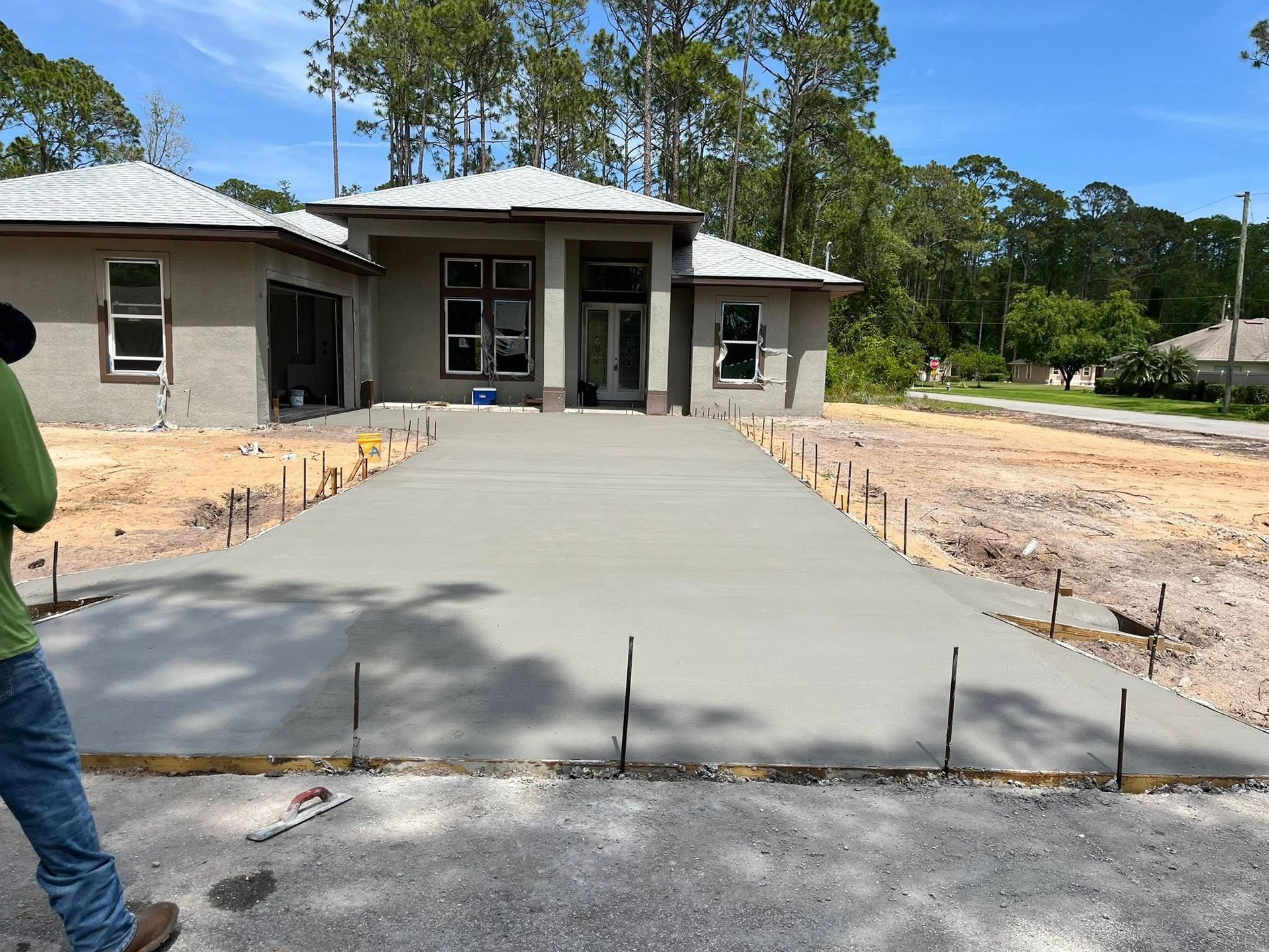 Newly poured concrete driveway leading to a house under construction; a worker stands at the side.