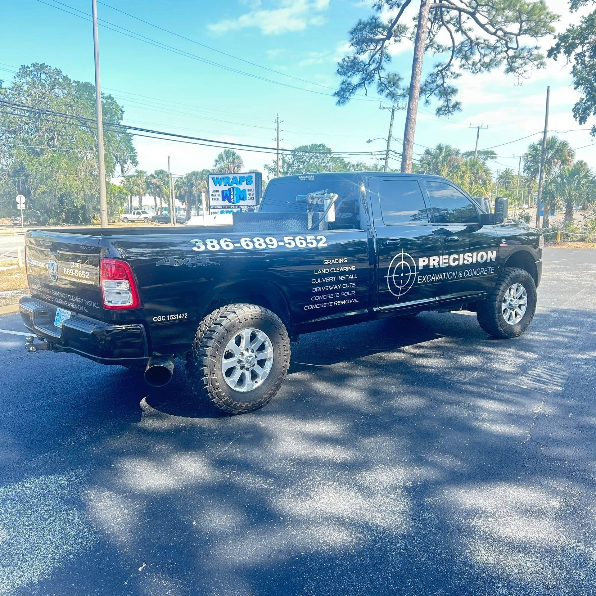 Black pickup truck with business logo and phone number, parked on pavement, sunny day.