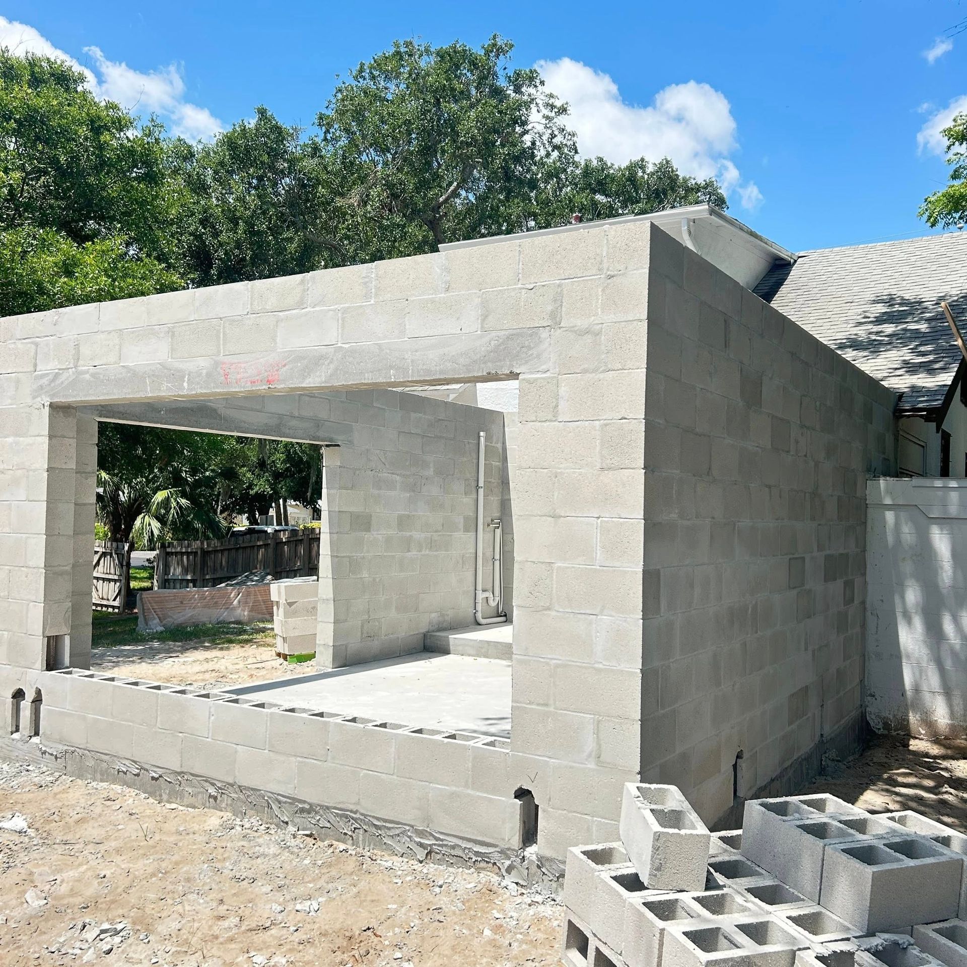 Construction of a gray concrete block building with open doorways, in a sunny outdoor setting.