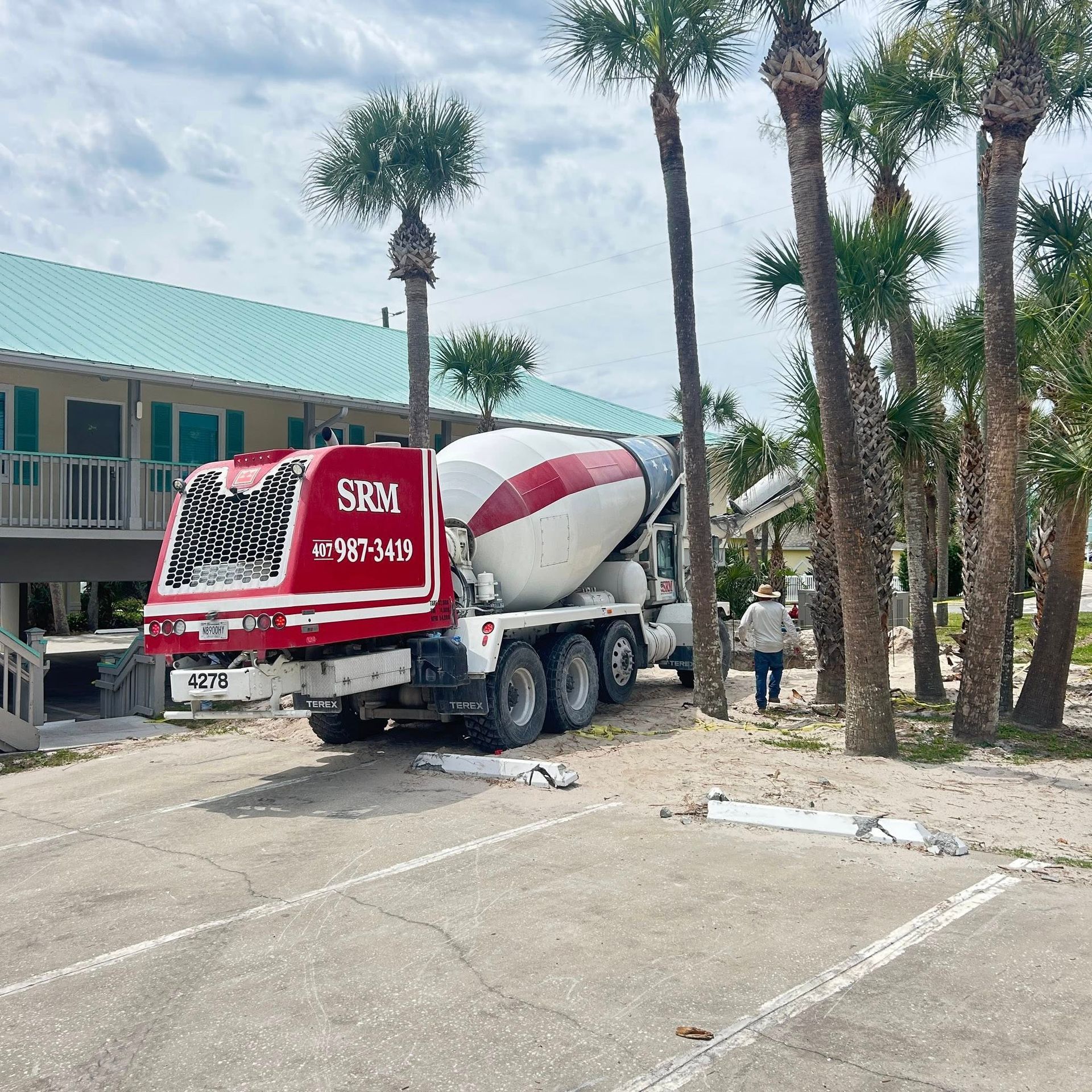 Red and white concrete truck parked in front of a building with palm trees and a person walking.