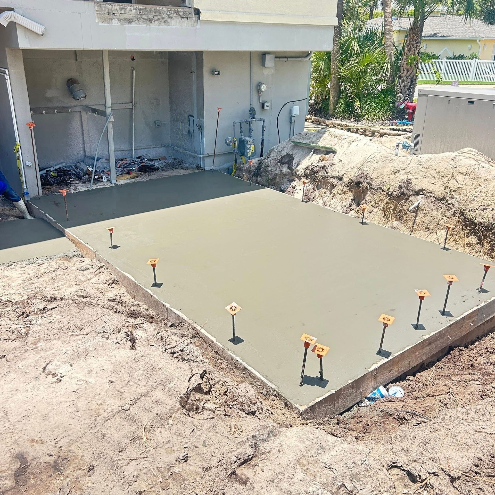 Freshly poured concrete patio; construction site. Gray concrete with orange stakes set in sandy soil.