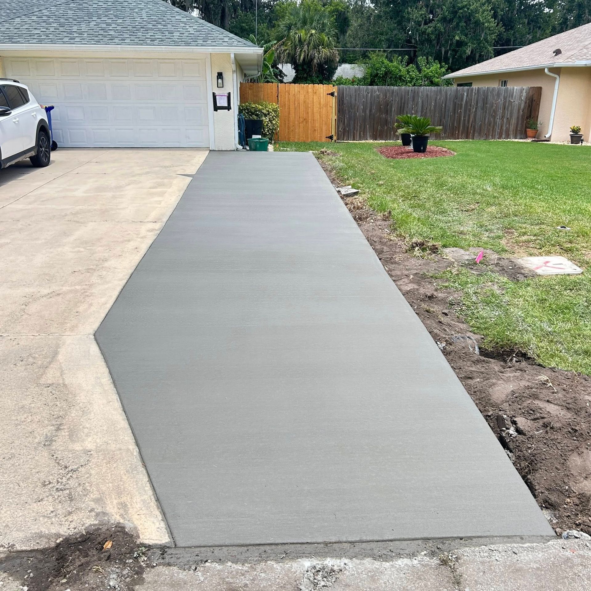 New concrete driveway in front of a house.  Driveway is gray, lawn is green, house is white.