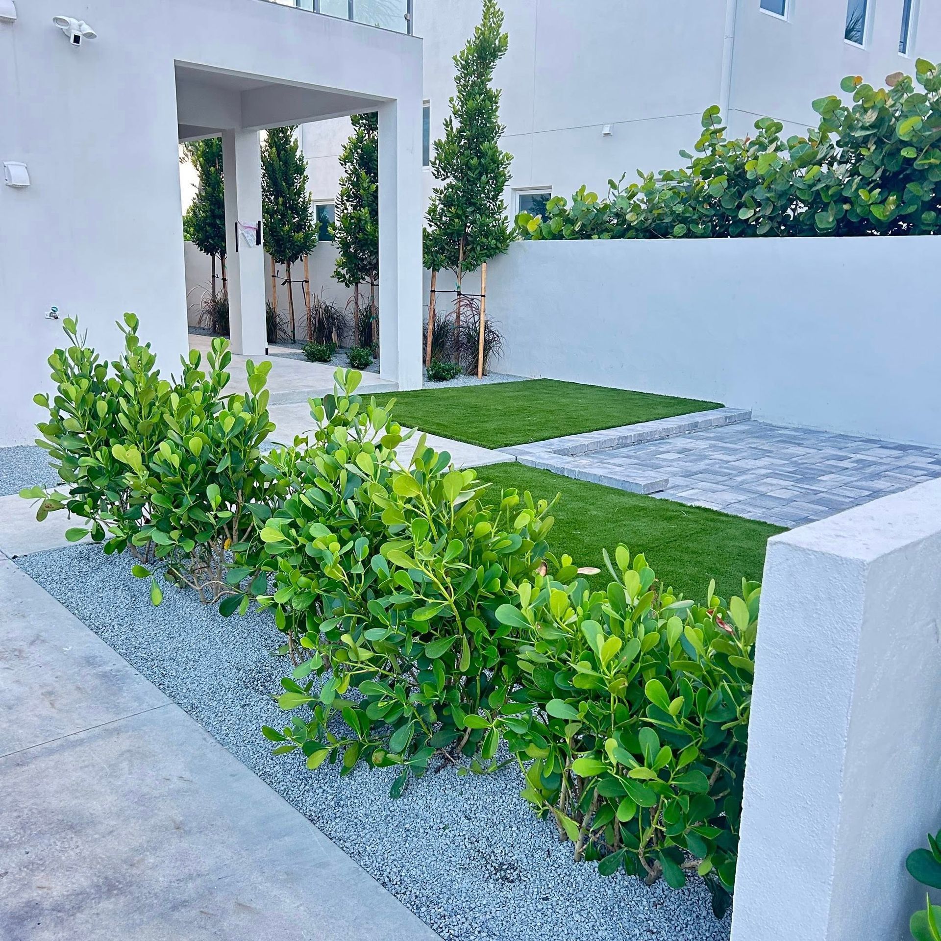 Exterior landscaping with green bushes, gravel, grass, and trees next to a white building.