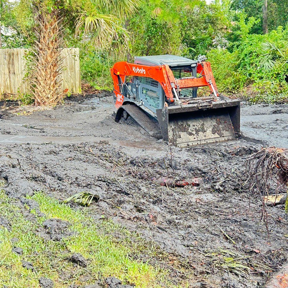 Orange Kubota skid steer stuck in muddy ground.