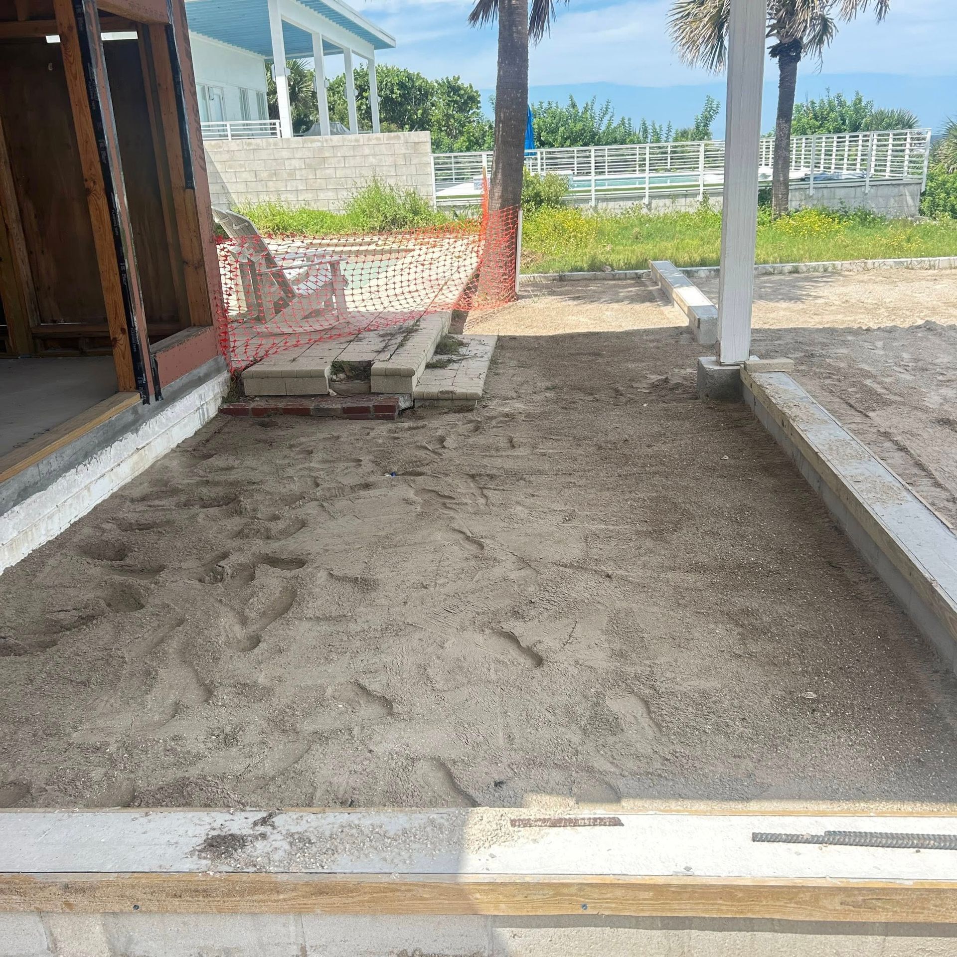 A sand-filled patio area with concrete borders, near a building and the beach.