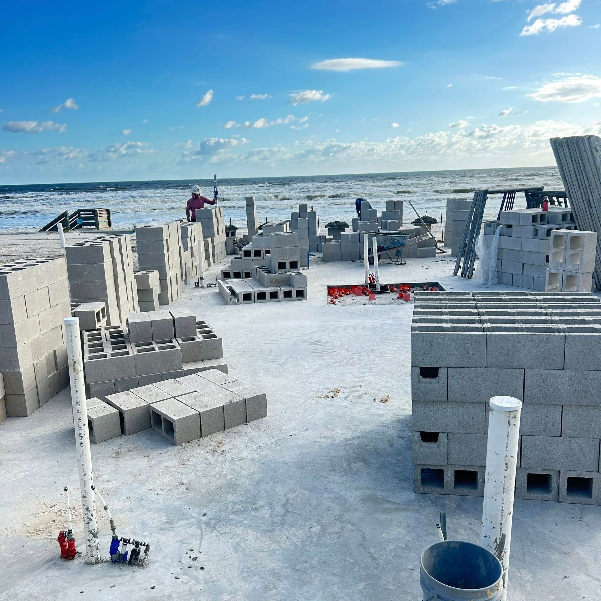 Construction on beach: gray cinder block structures. People work amid the blocks near the ocean.