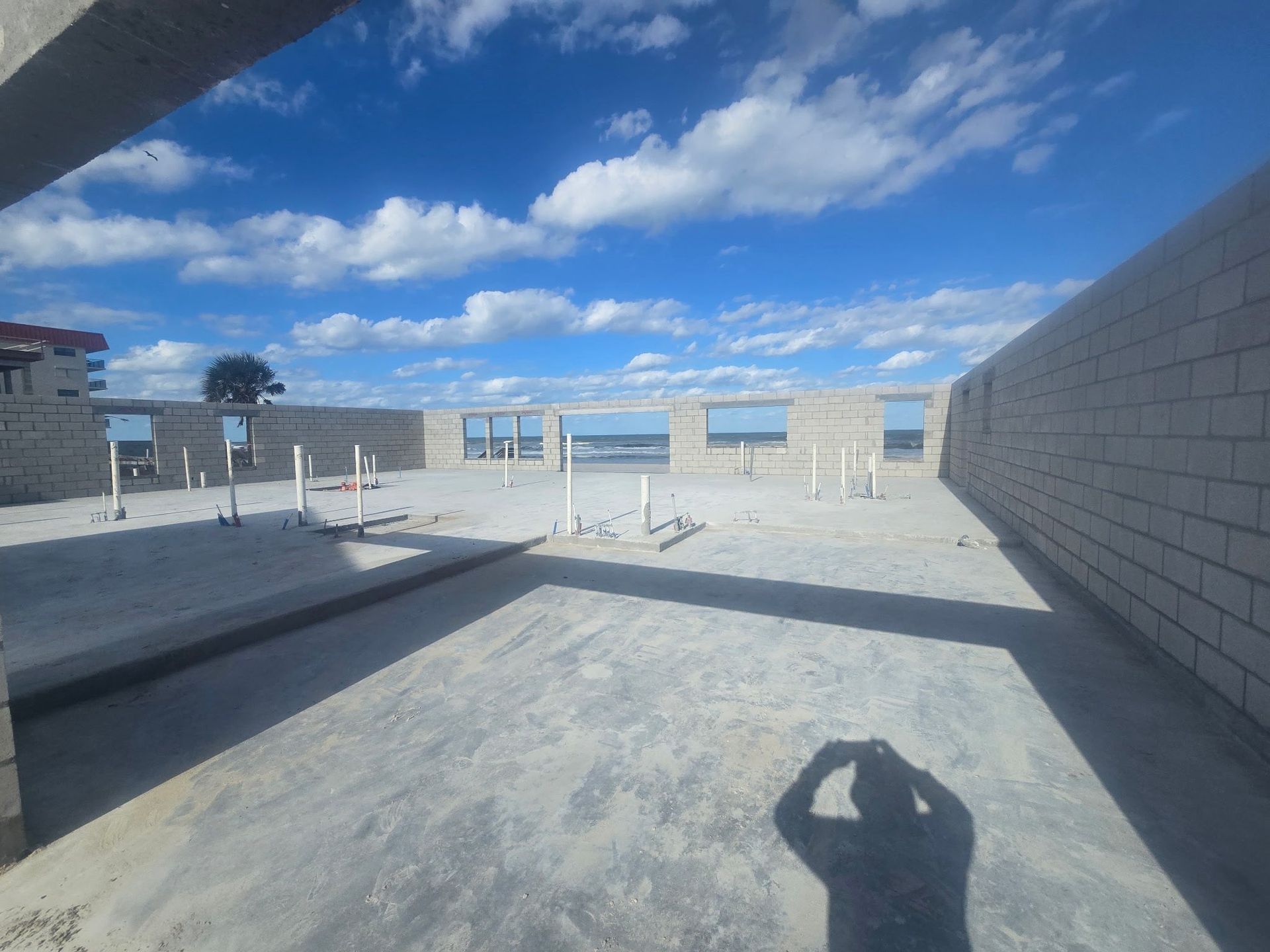 Interior of a building under construction, concrete walls and floor, blue sky visible through window frames.