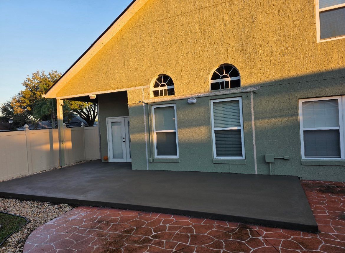 A concrete patio outside a stucco house; a decorative stone border and a fence are also visible.