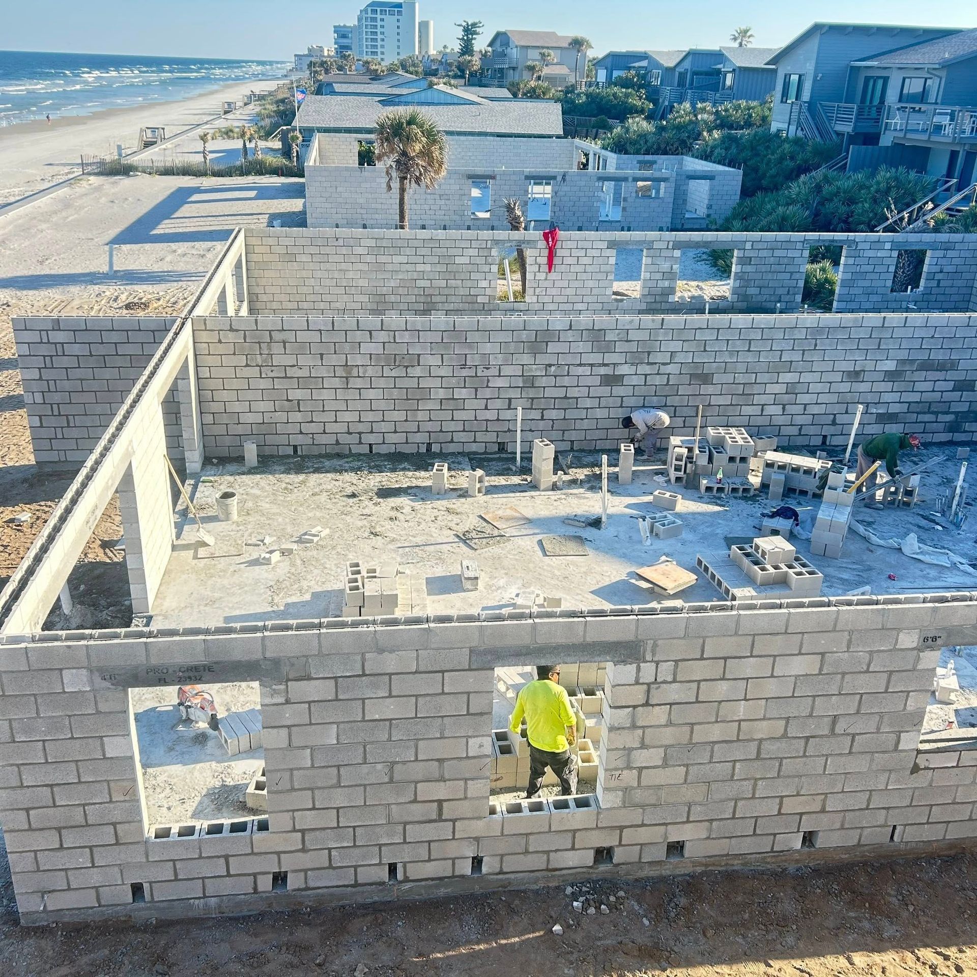Construction of concrete block buildings near a beach. A worker stands in a doorway, several unfinished structures visible.