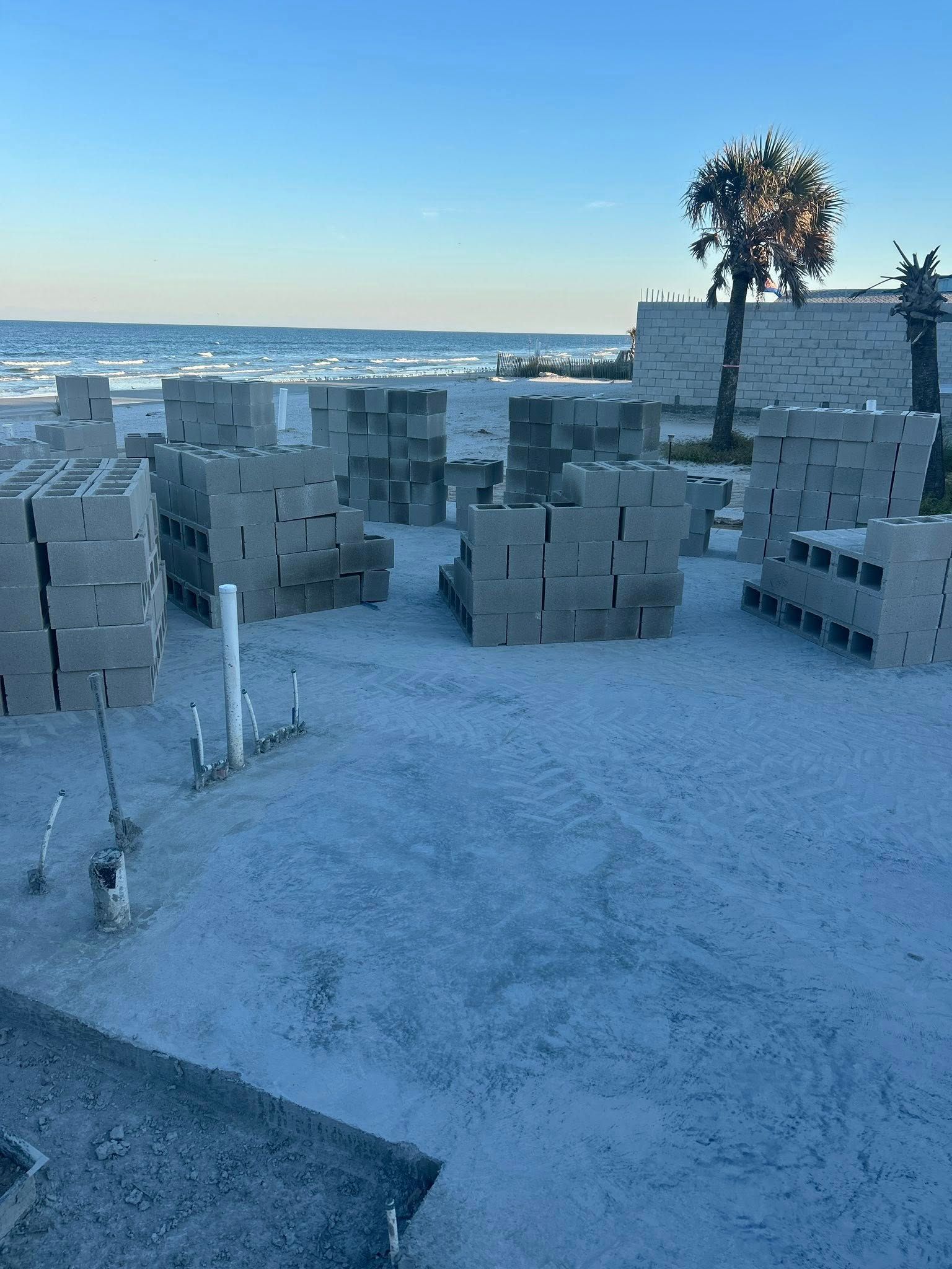 Stacks of concrete blocks on a sandy beach, with the ocean in the background under a blue sky.