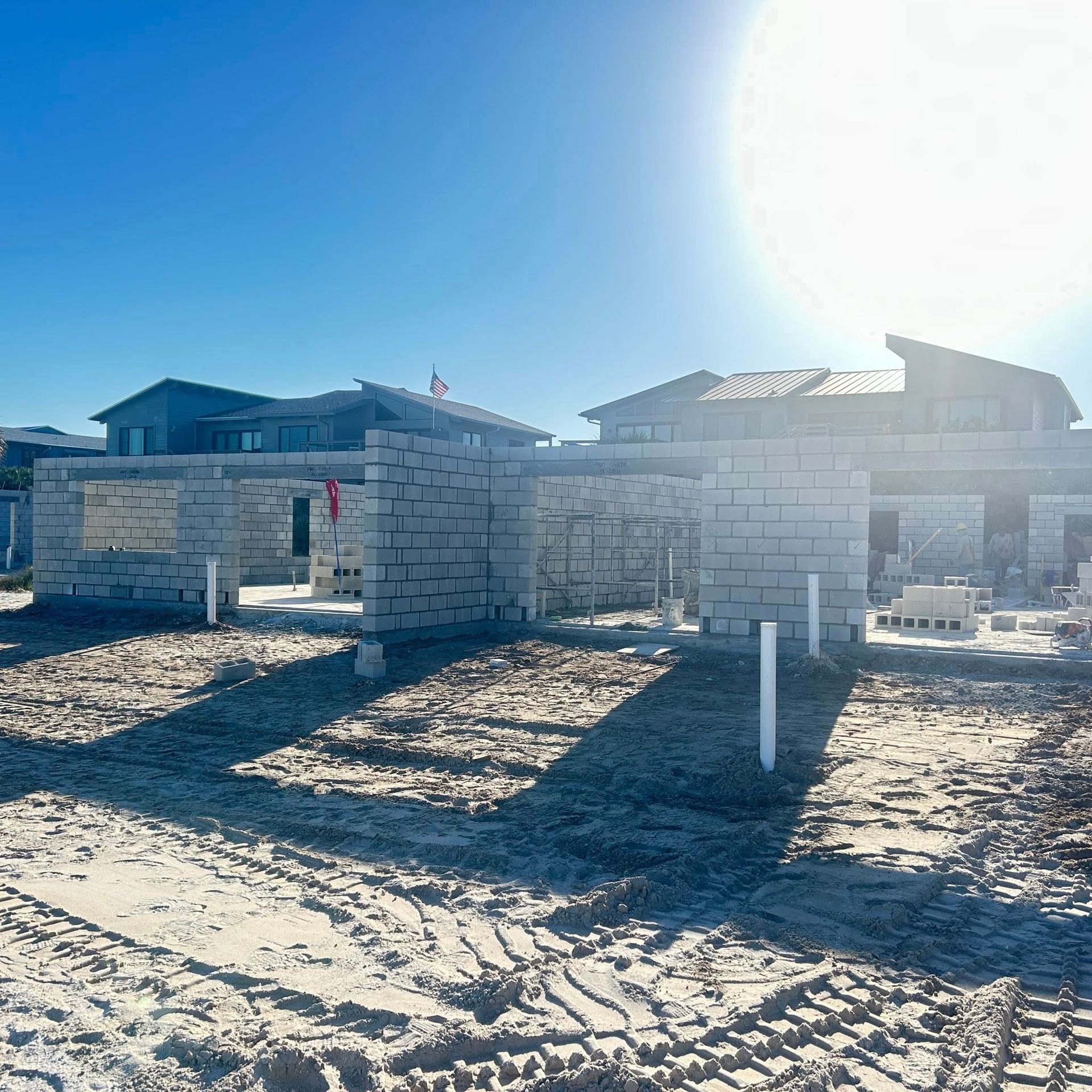 Construction site with concrete block walls in progress; sunny sky, beach-like setting.