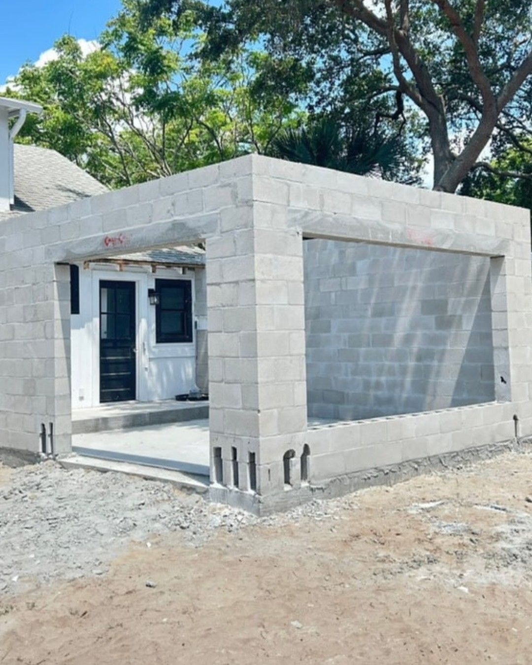Construction of a concrete block structure with an open front and large rectangular window opening; light gray blocks.
