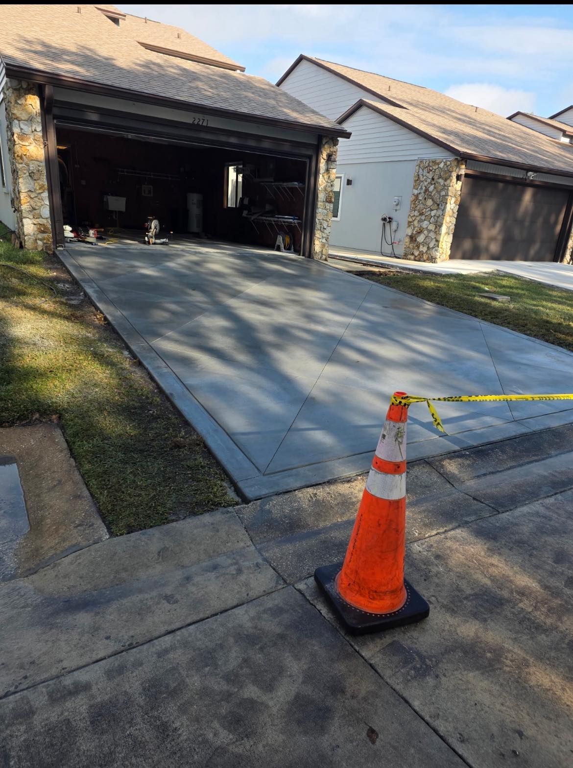 Newly poured concrete driveway with orange cone and caution tape.