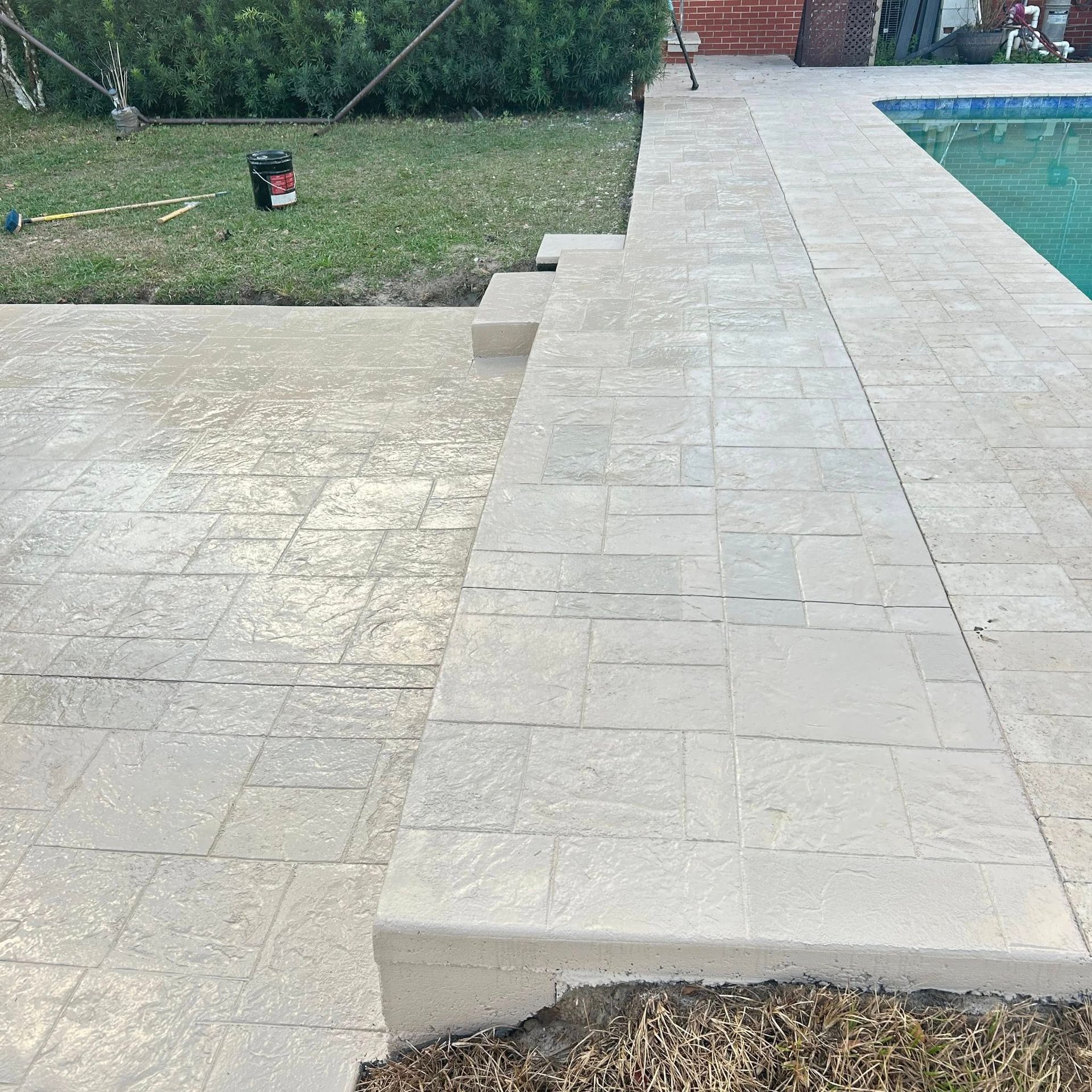Concrete pool deck with steps and green grass.