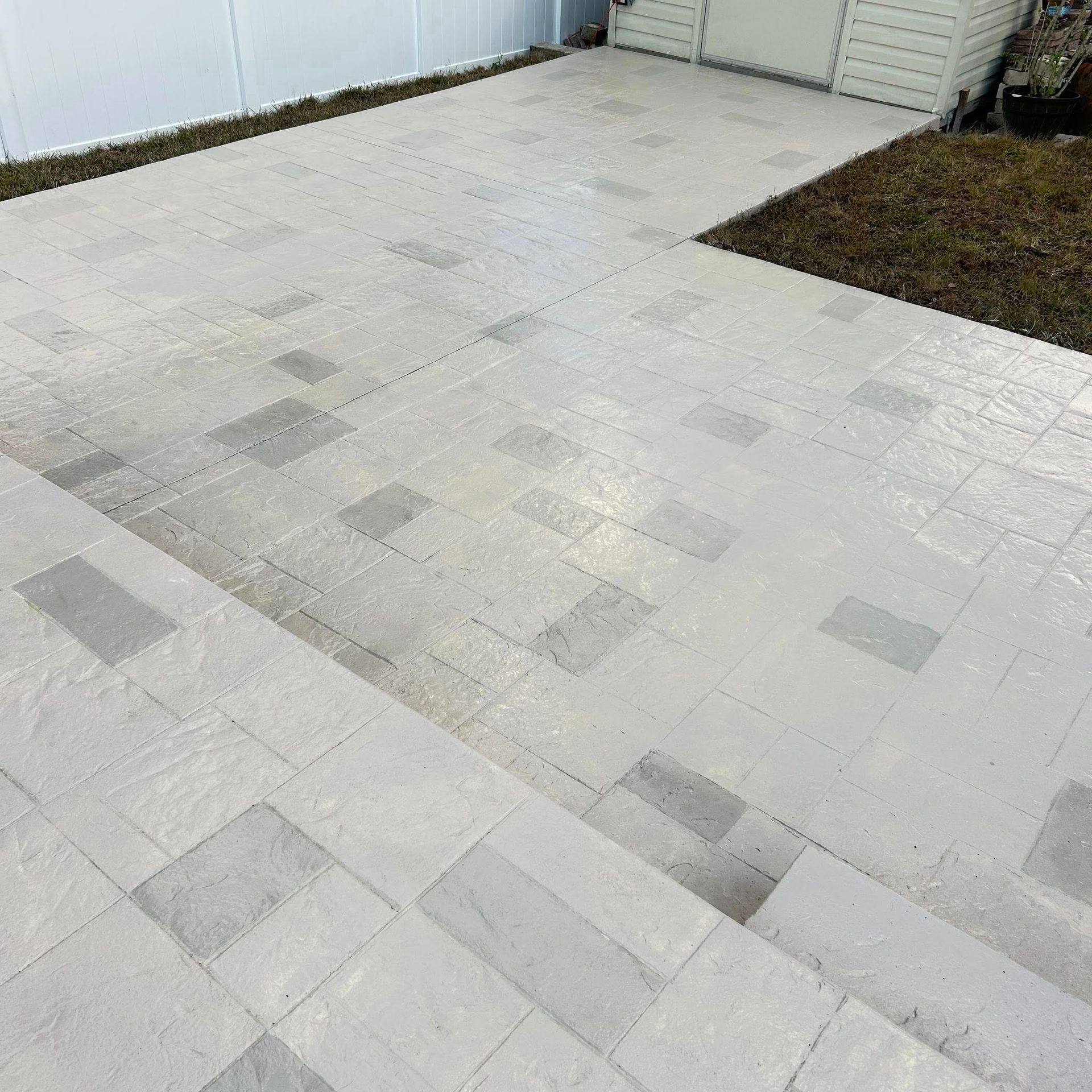 Light gray stone patio with darker gray accents and a small shed in the background.