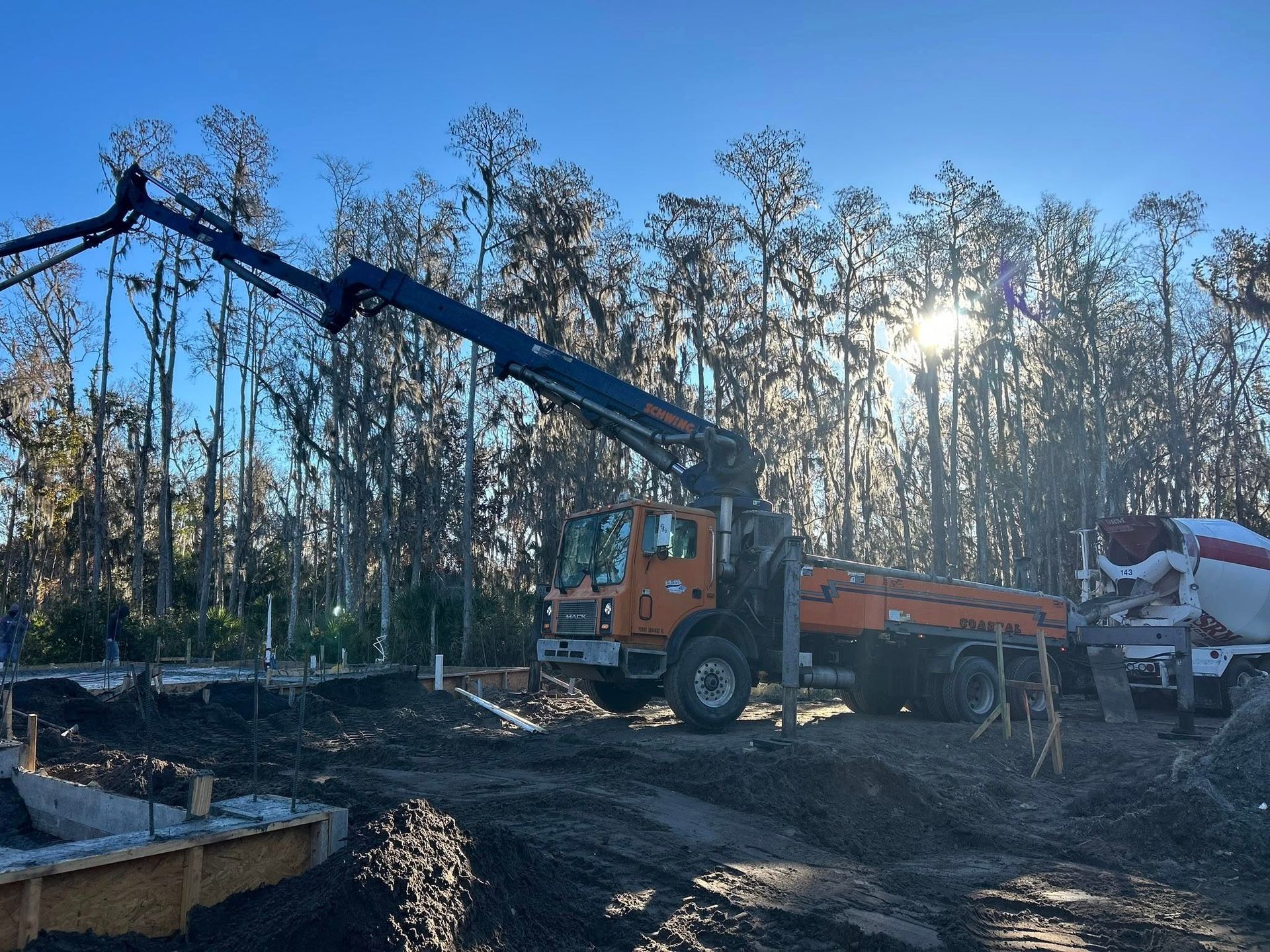 Concrete pump truck pouring concrete at a construction site in front of a forest with sunlight.