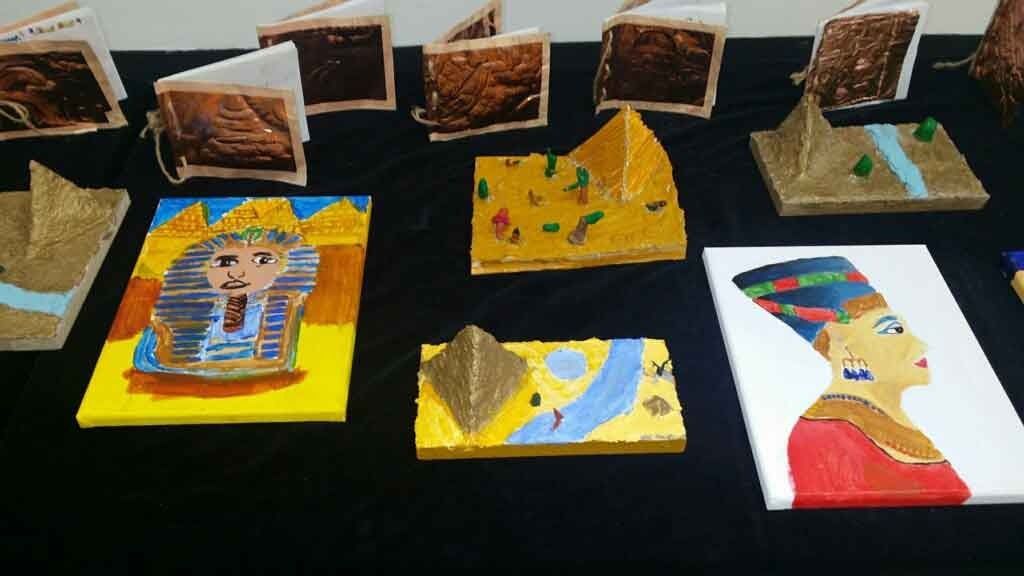 An exhibit table displays student artwork of ancient Egypt, featuring paintings of King Tut and Nefertiti, 3D pyramid models, and handmade books.