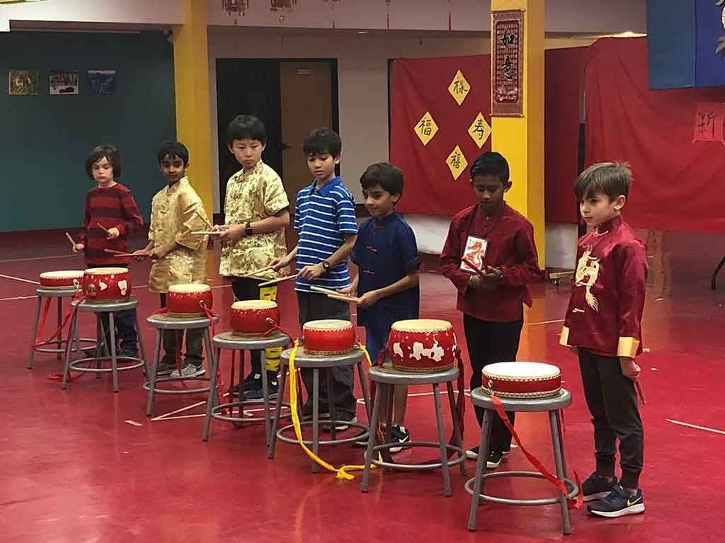A group of Montessori elementary students perform a traditional Chinese drumming routine with red festive drums during a school cultural celebration.