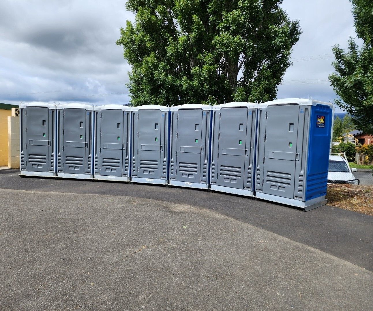 Row of Grey Portable Toilets Outdoors Beside a Paved Area — Wee R Portable Loos in Glenorchy, TAS