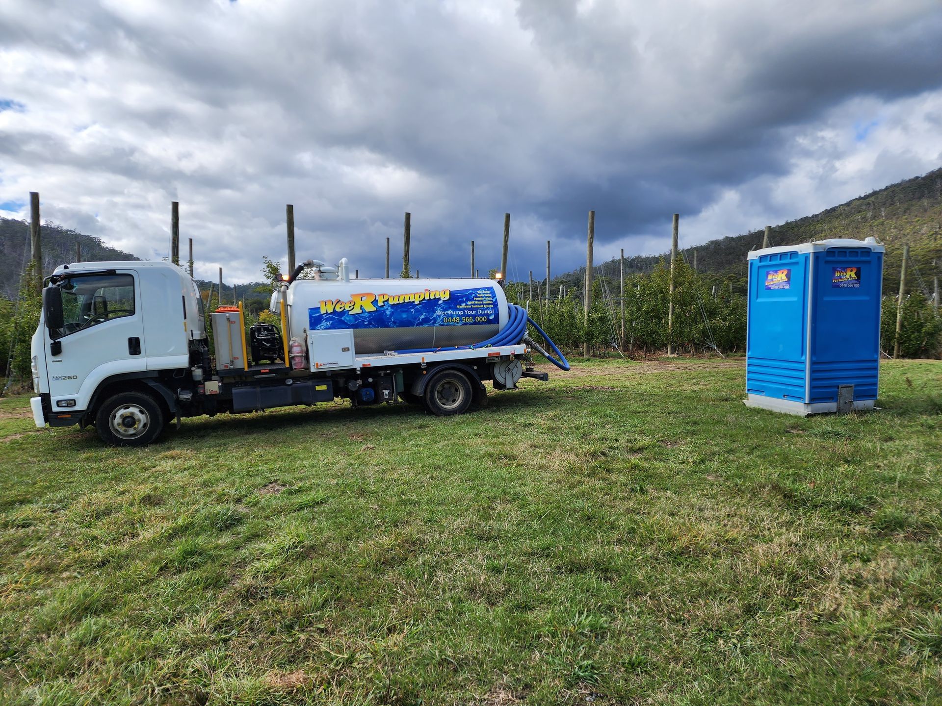 White tanker truck in a grassy field near two blue portable toilets under cloudy skies  Wee R Portable Loos in Glenorchy, TAS