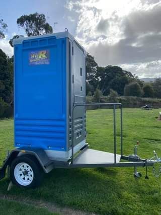 Blue Portable Toilet On A Trailer In A Grassy Field Under Cloudy Sky — Wee R Portable Loos in Glenorchy, TAS