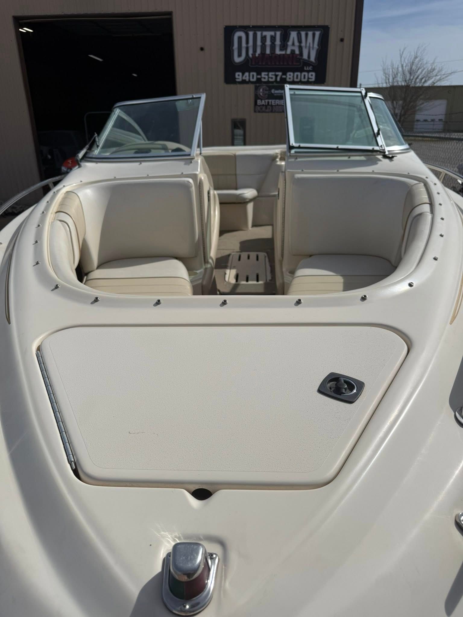 White boat cockpit with cream seats and open windshield, shown parked outside a shop.