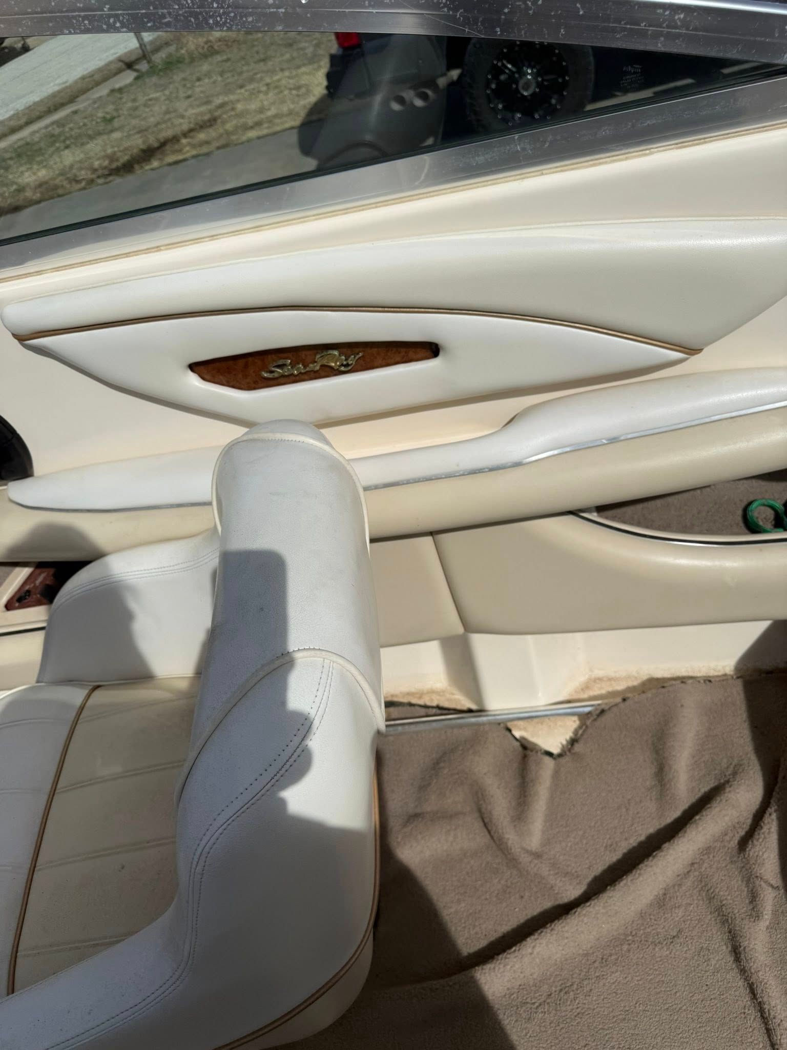 Inside a car, white leather seat and door panel with wood trim and a window view.