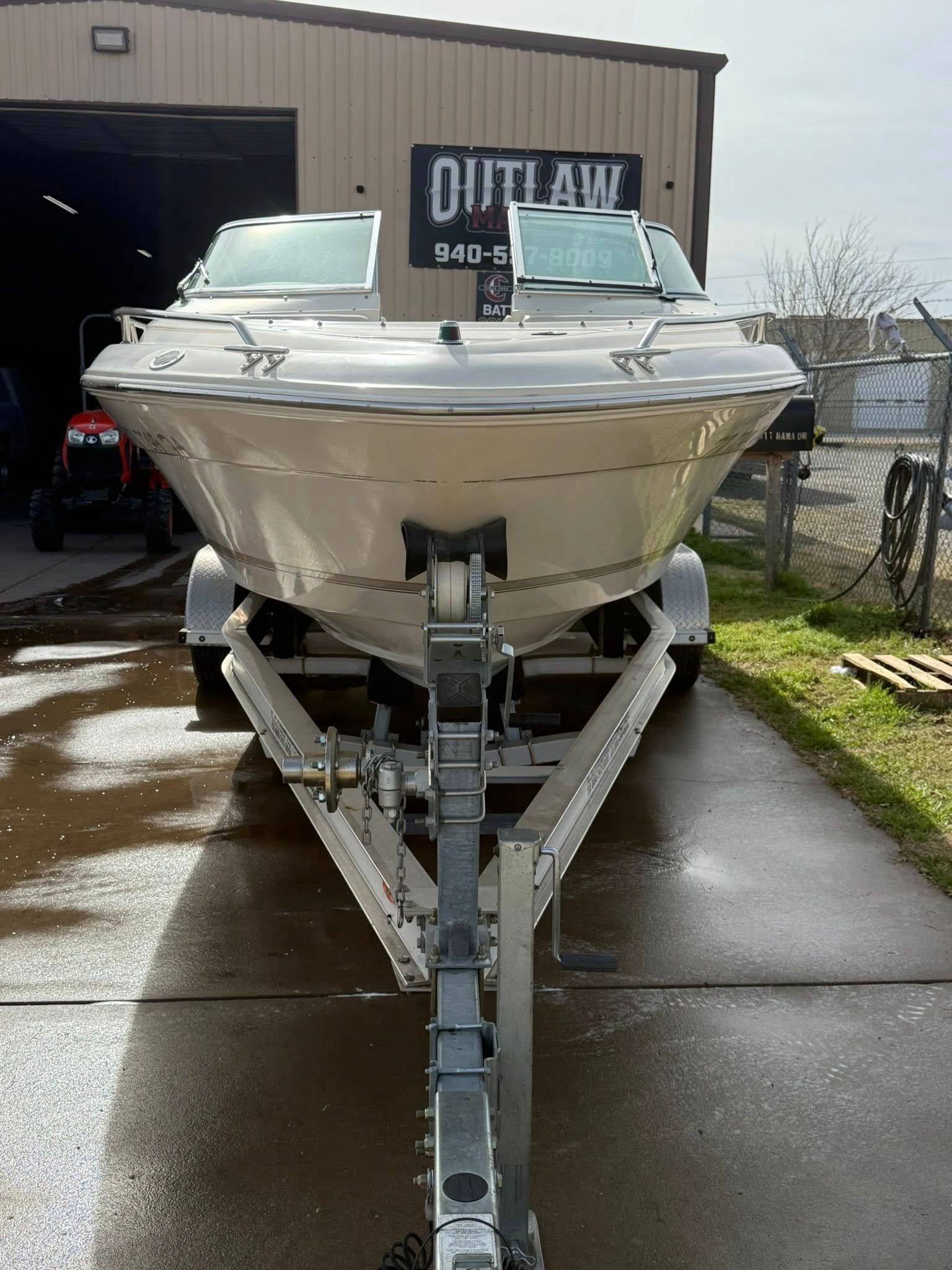 White speedboat on a trailer in a driveway outside a workshop