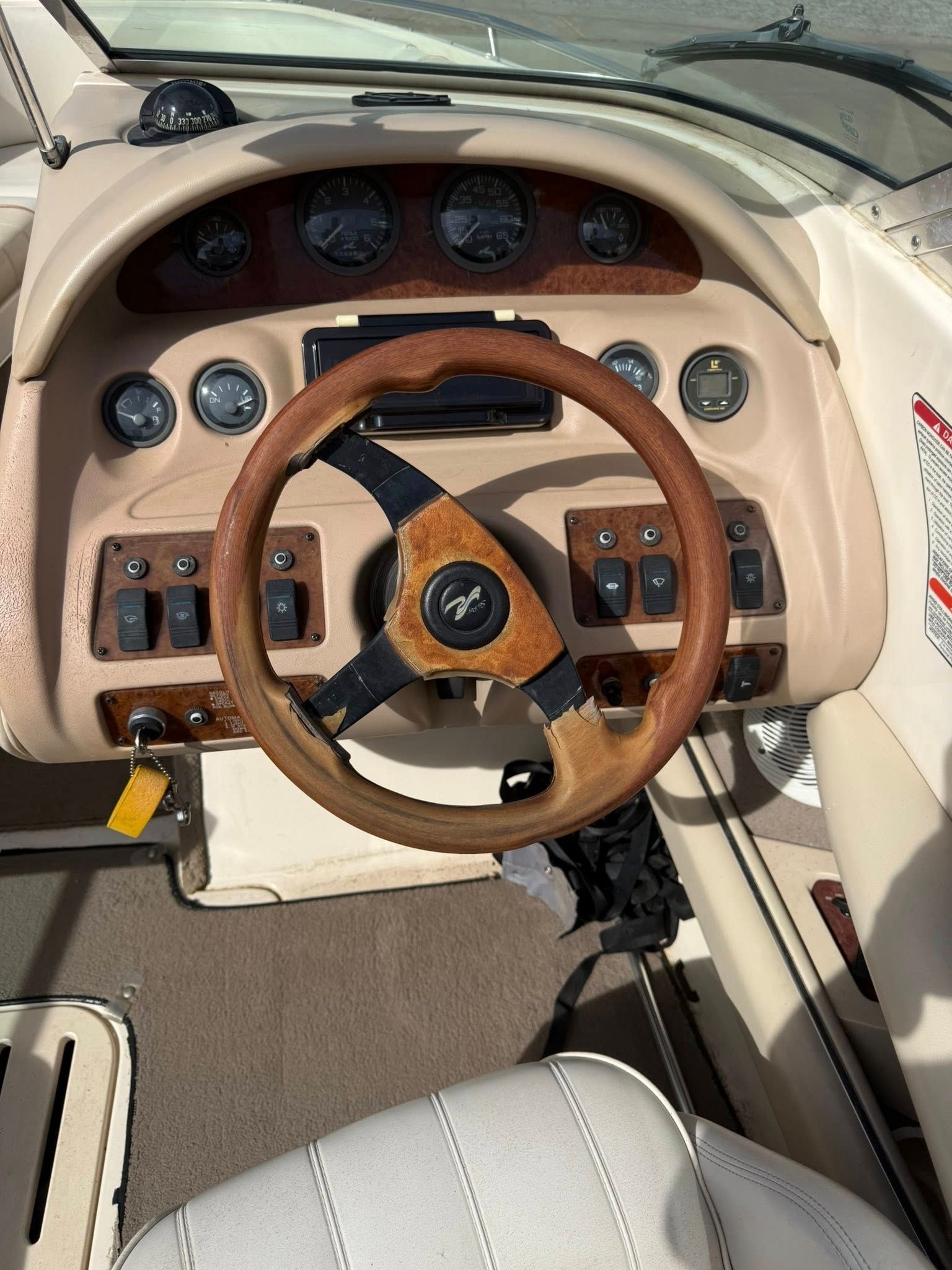 Boat cockpit with tan dashboard, wood steering wheel, and instrument gauges centered on the helm.