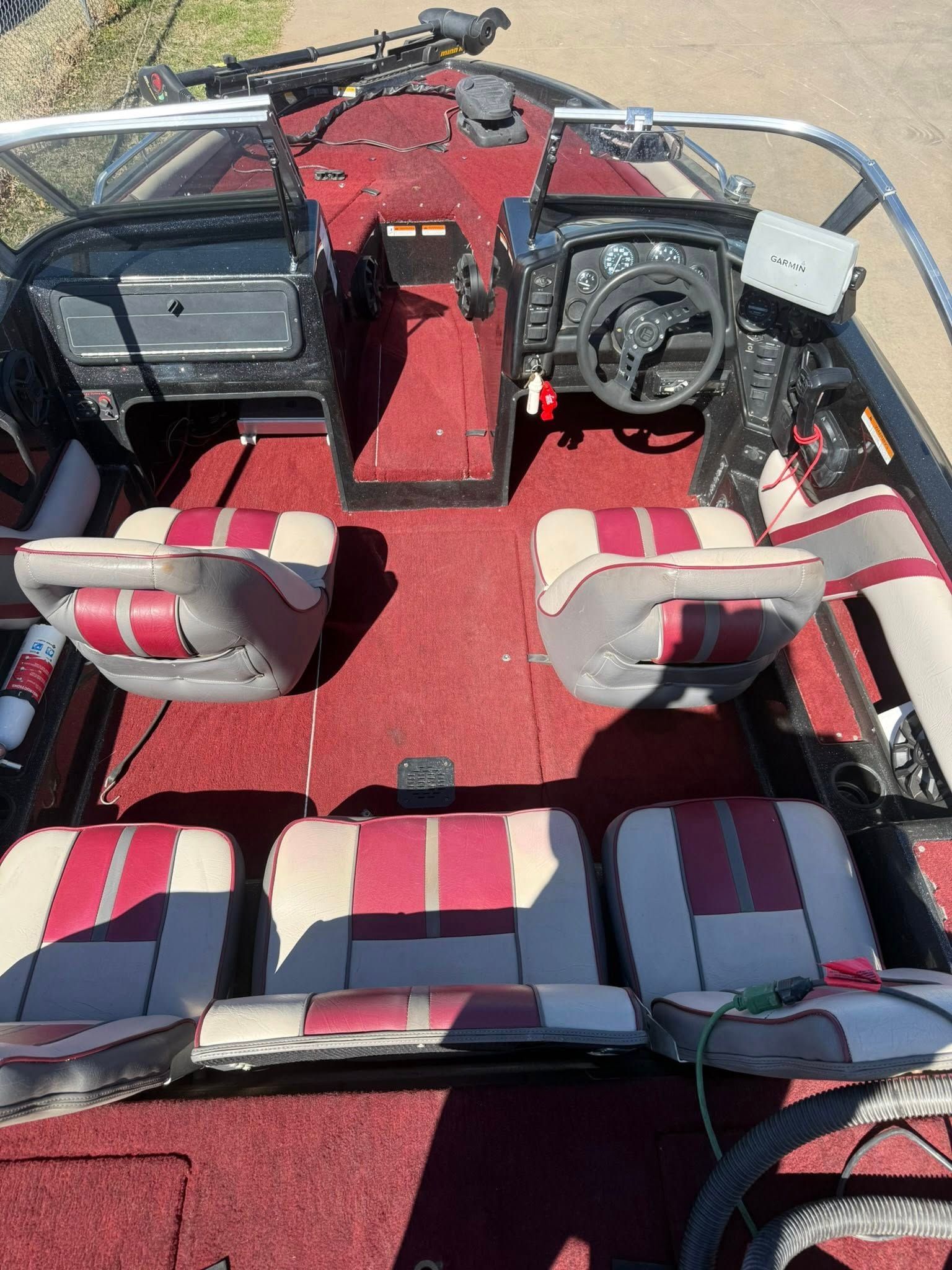 Boat cockpit with red carpet, striped seats, steering wheel, and windshield on a sunny day
