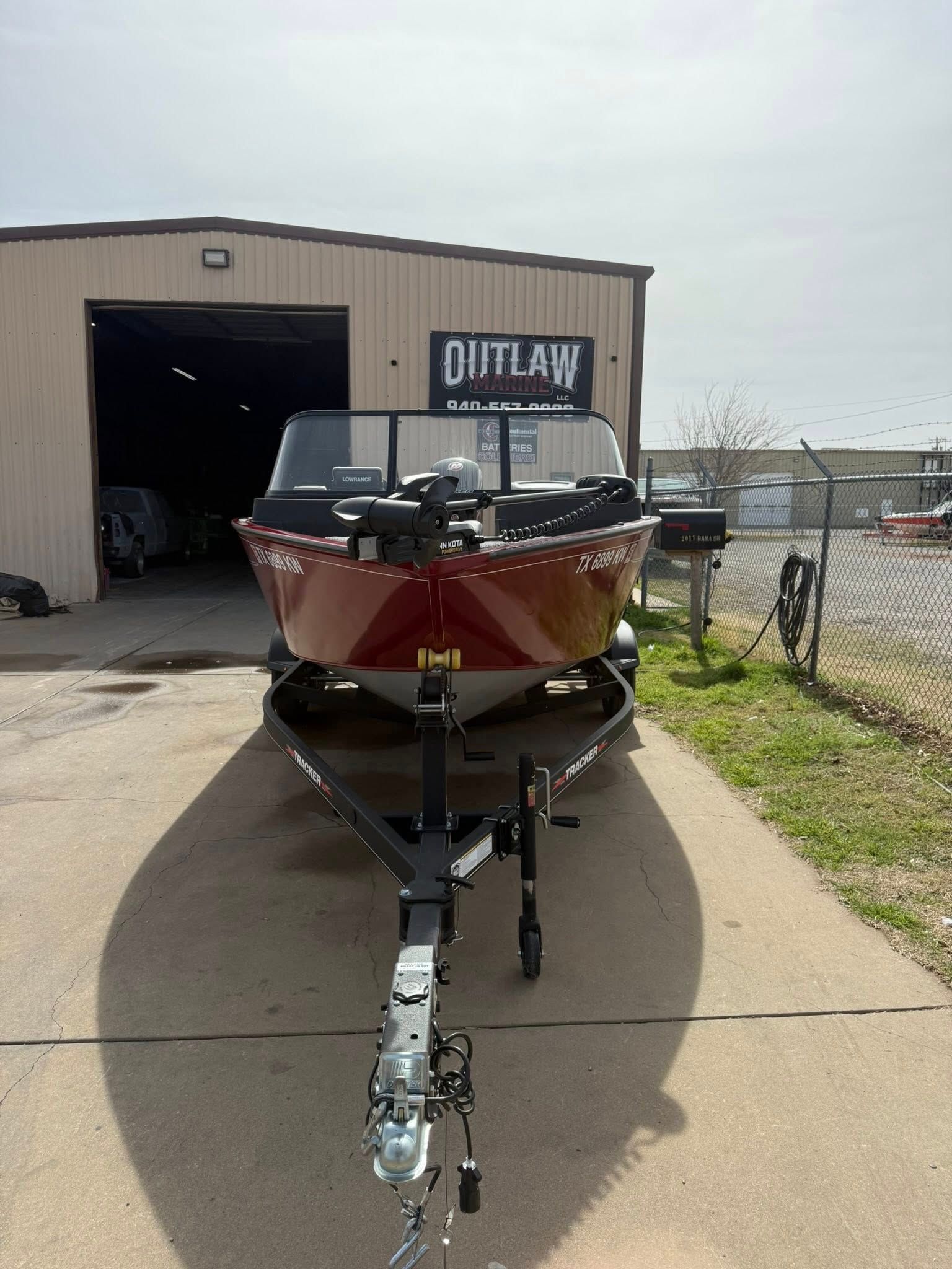 Red boat on a trailer parked outside a metal garage building