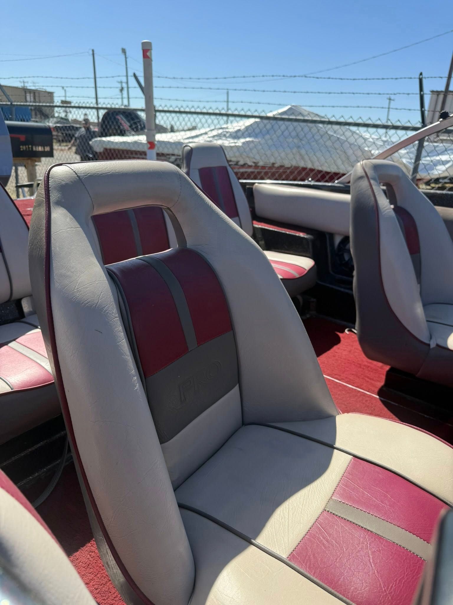 Boat seats with red-and-gray upholstery under bright sunlight on a deck by the water