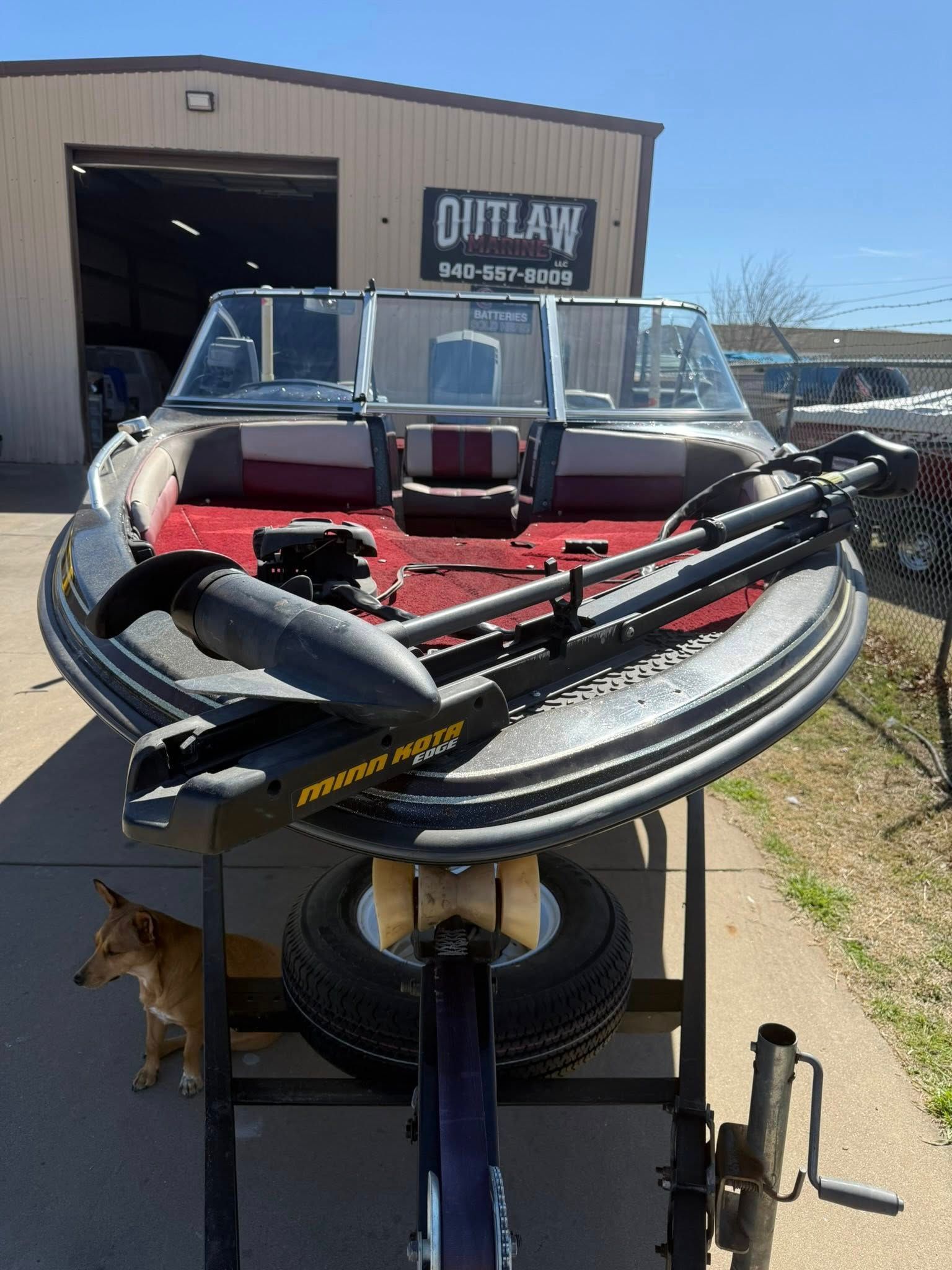 Fishing boat on trailer in front of a garage, with a red deck, trolling motor, and gear on the bow