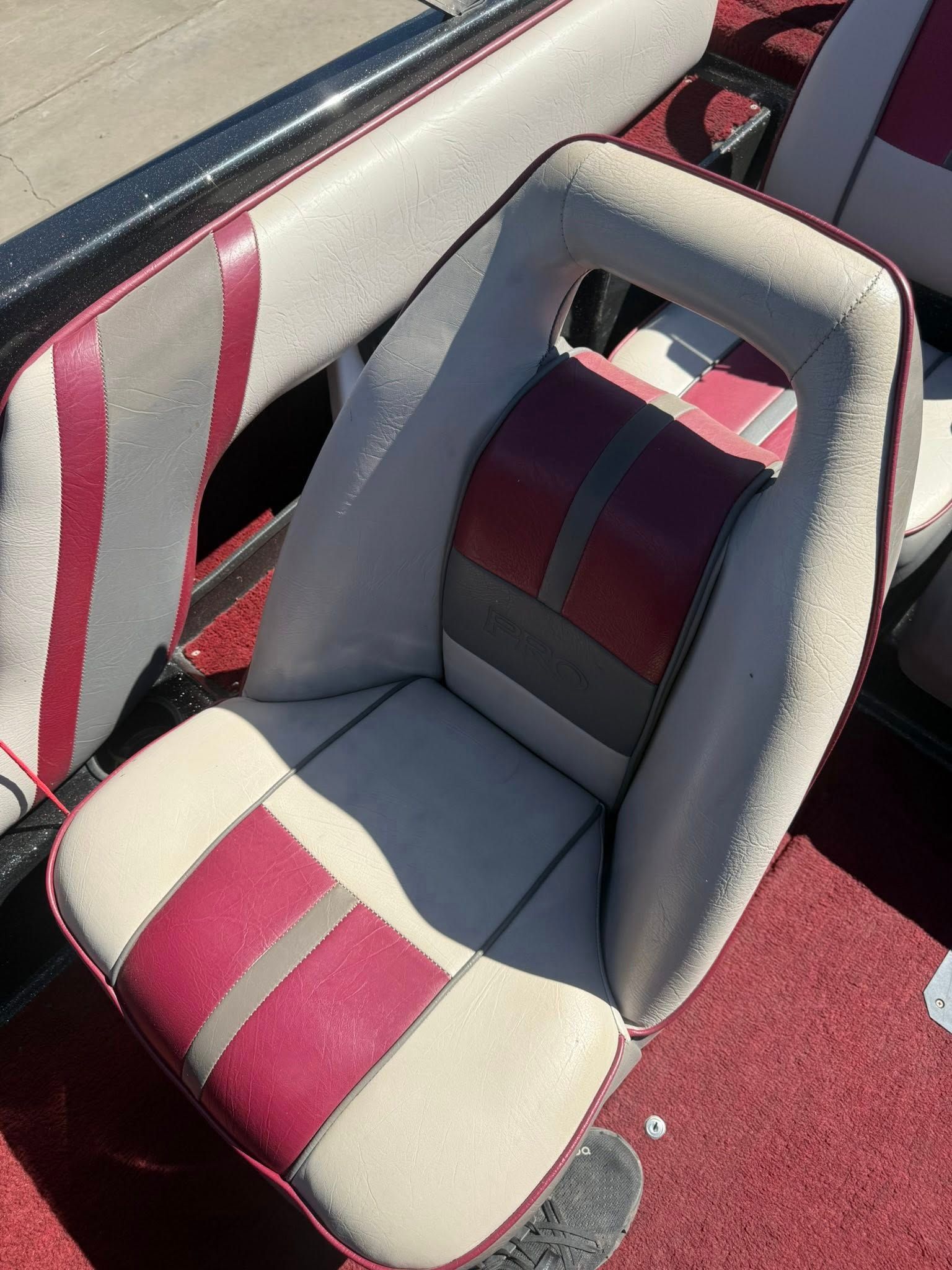Padded boat seat with gray and burgundy upholstery beside a matching backrest and carpeted deck