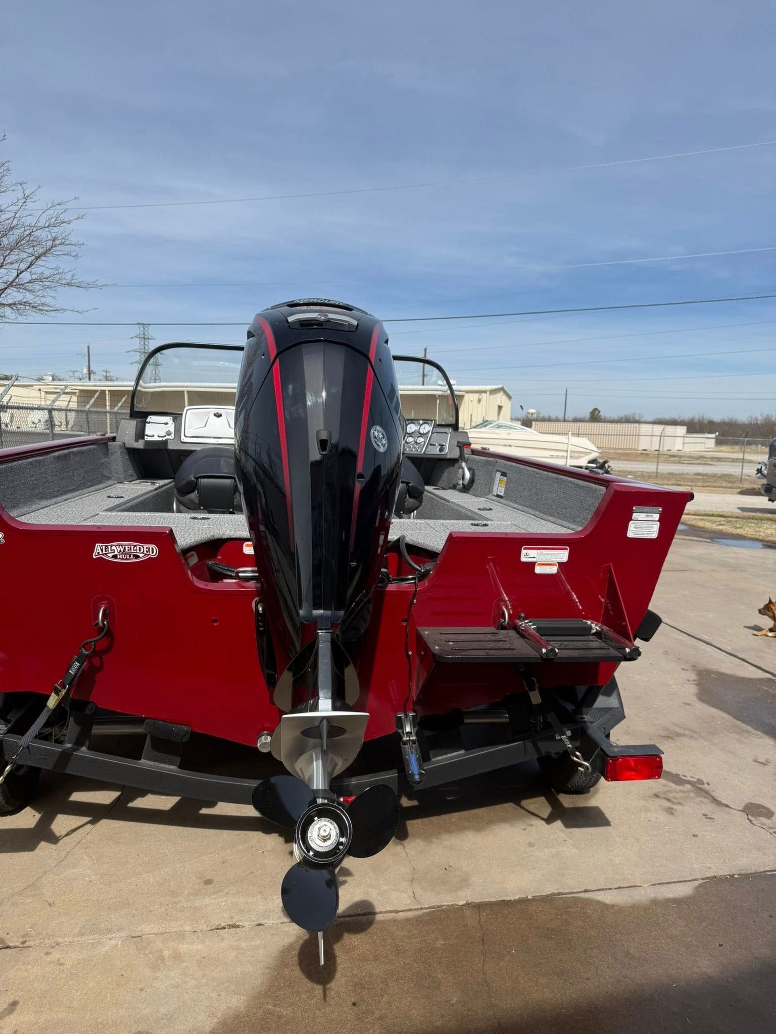 Red fishing boat with black outboard motor on a trailer at a waterfront lot under a blue sky