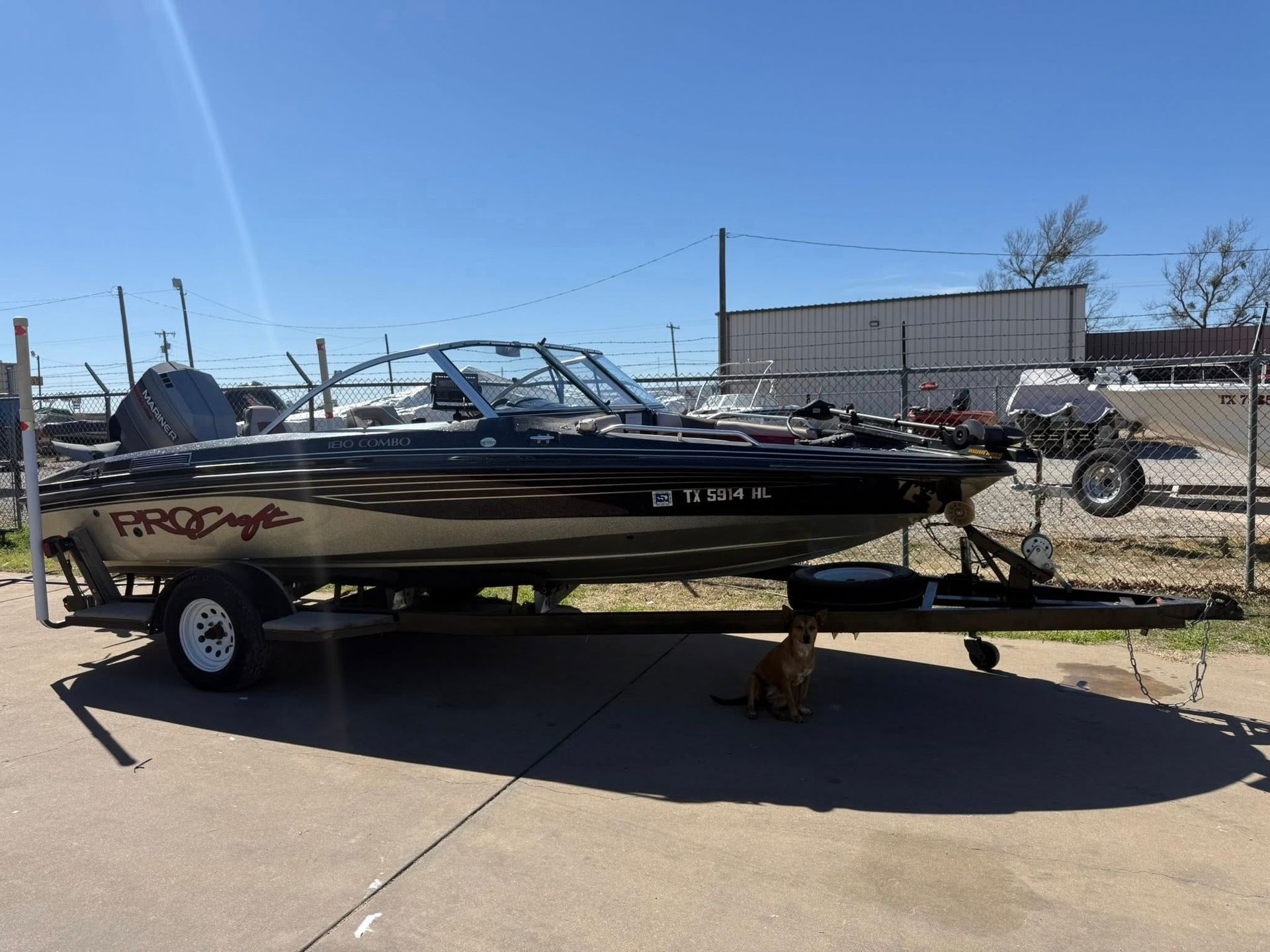 Black fishing boat on a trailer in a parking lot under a clear blue sky