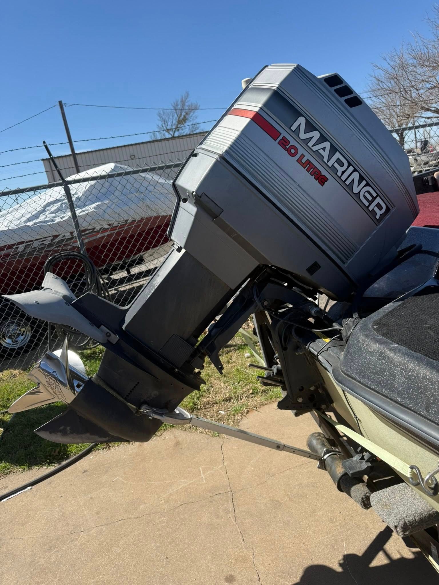 Overturned white and gray marine motorboat leaning on its side in a fenced yard
