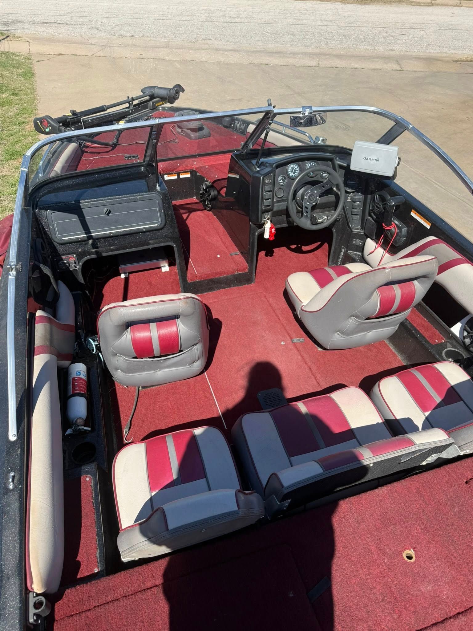 Red boat cockpit with red carpet, two seats, steering wheel, and folded shade canopy.
