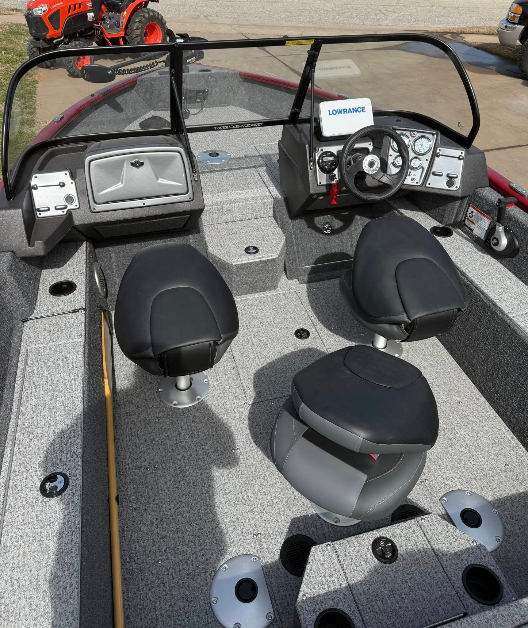 Fishing boat helm with two black seats, steering wheel, and console on a gray deck