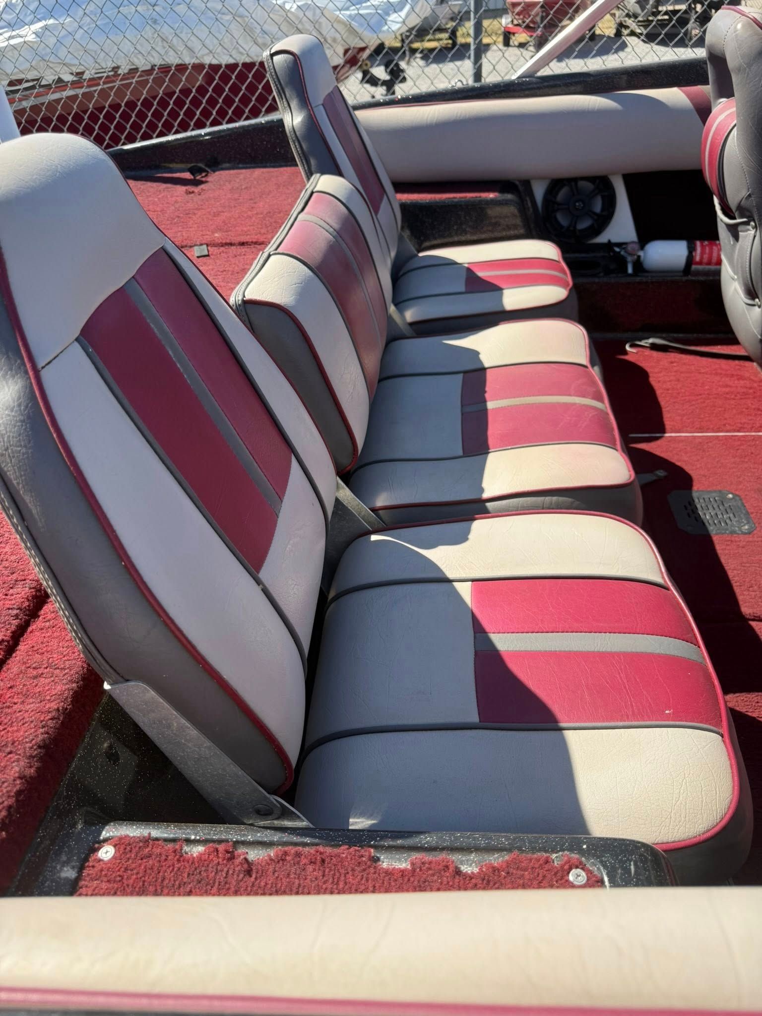 Red and gray cushioned boat seats on a red carpeted deck with a windshield in the background