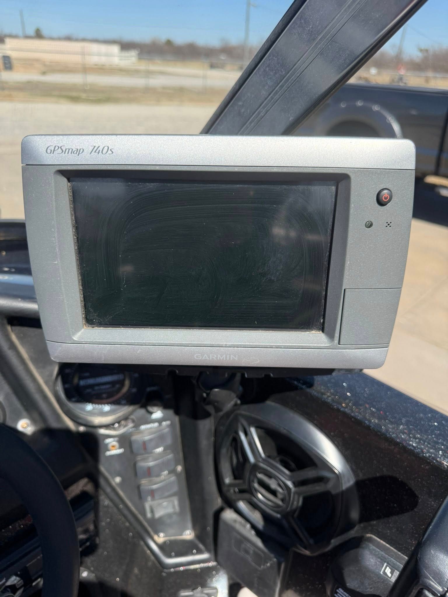 Gray touchscreen device mounted in a vehicle cabin, with a black screen and a small red indicator light.