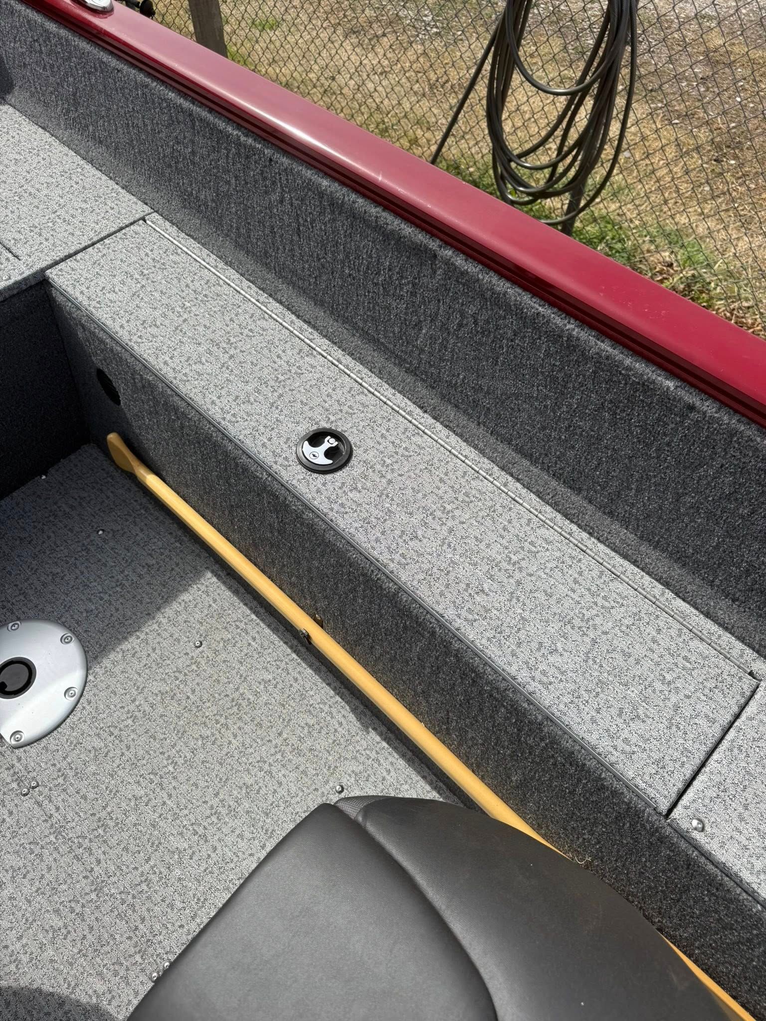 Close-up of a gray boat interior with a black seat, red trim, and a yellow rod along the side.