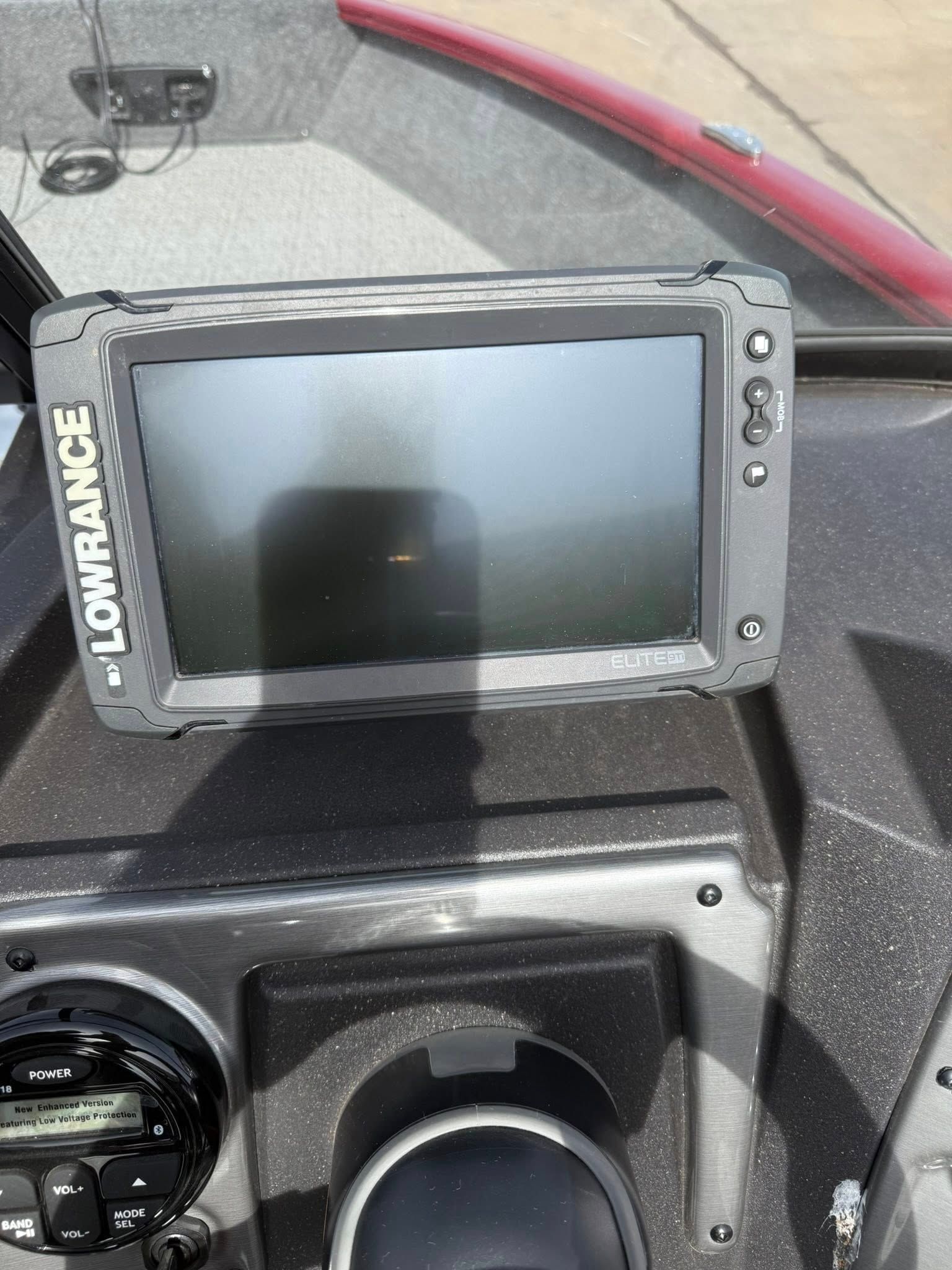 Lowrance fish finder mounted on a boat dashboard, screen off, with windshield reflection.