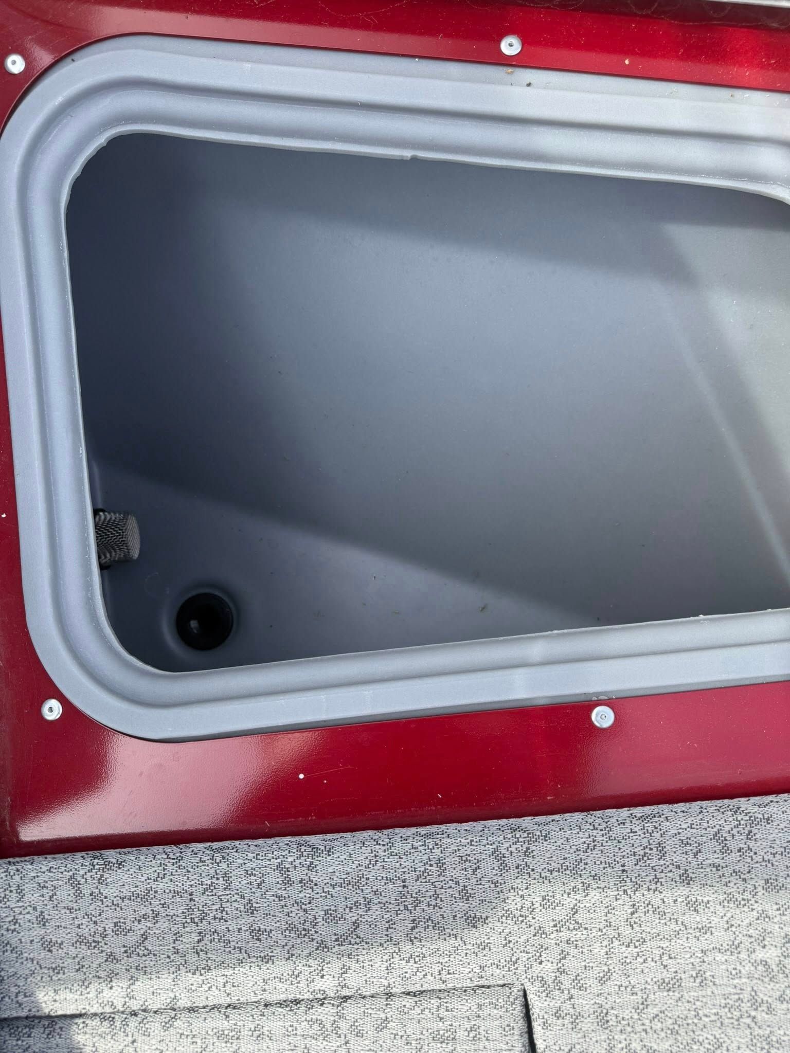 Gray empty storage compartment with a black drain opening in a red vehicle or boat surface