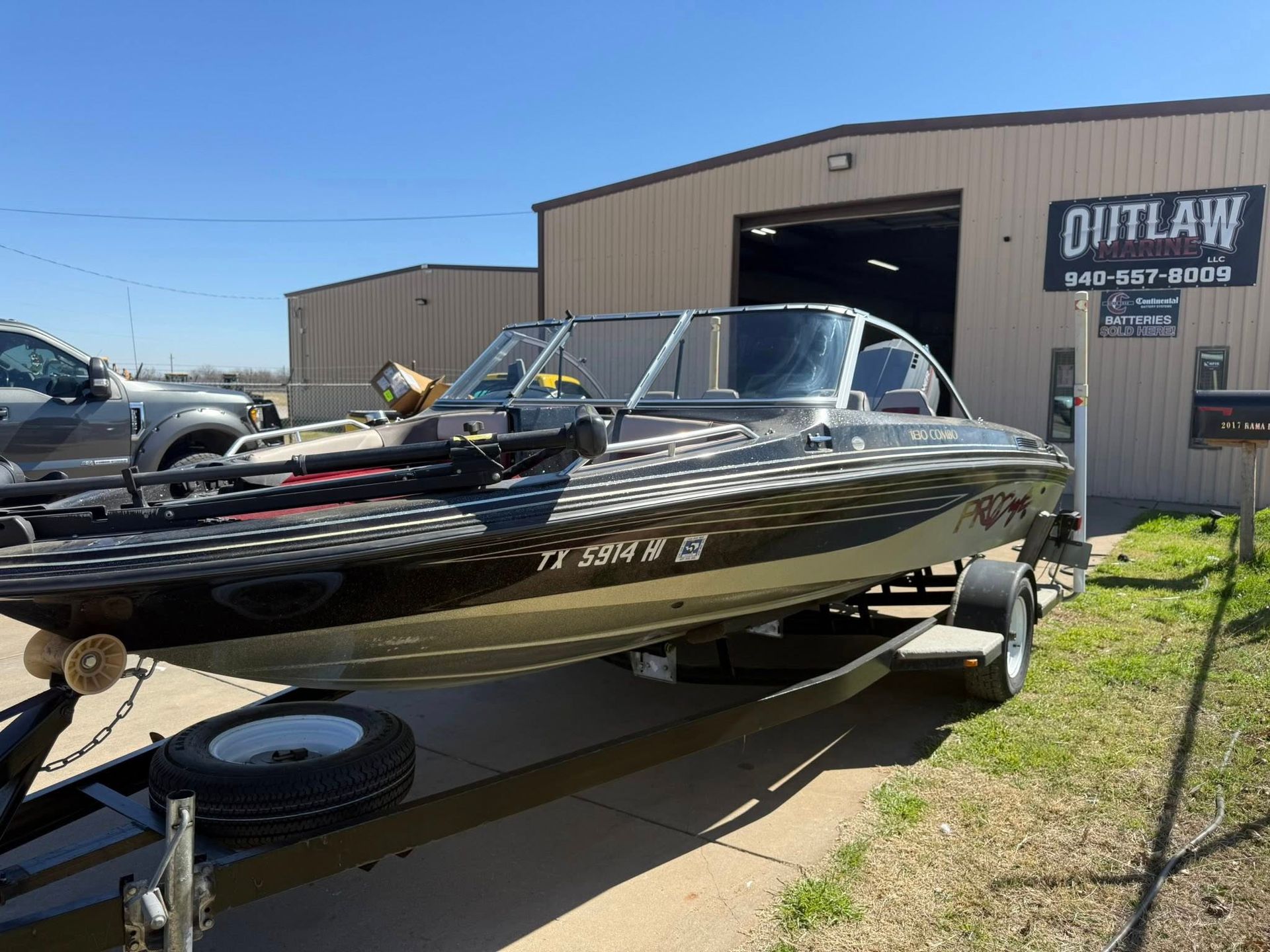 Black and silver fishing boat on a trailer outside a boat shop in bright sunlight