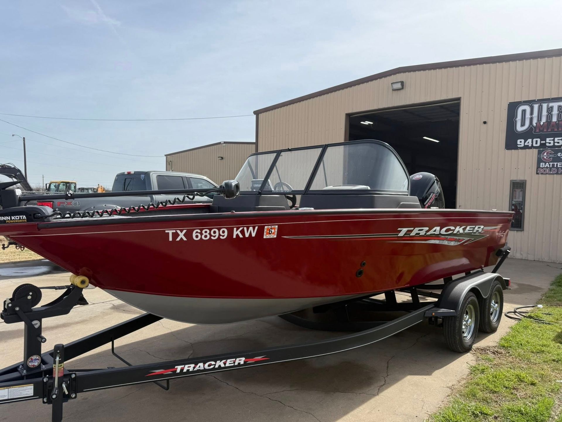 Red Tracker boat on trailer parked outside a shop in daylight.