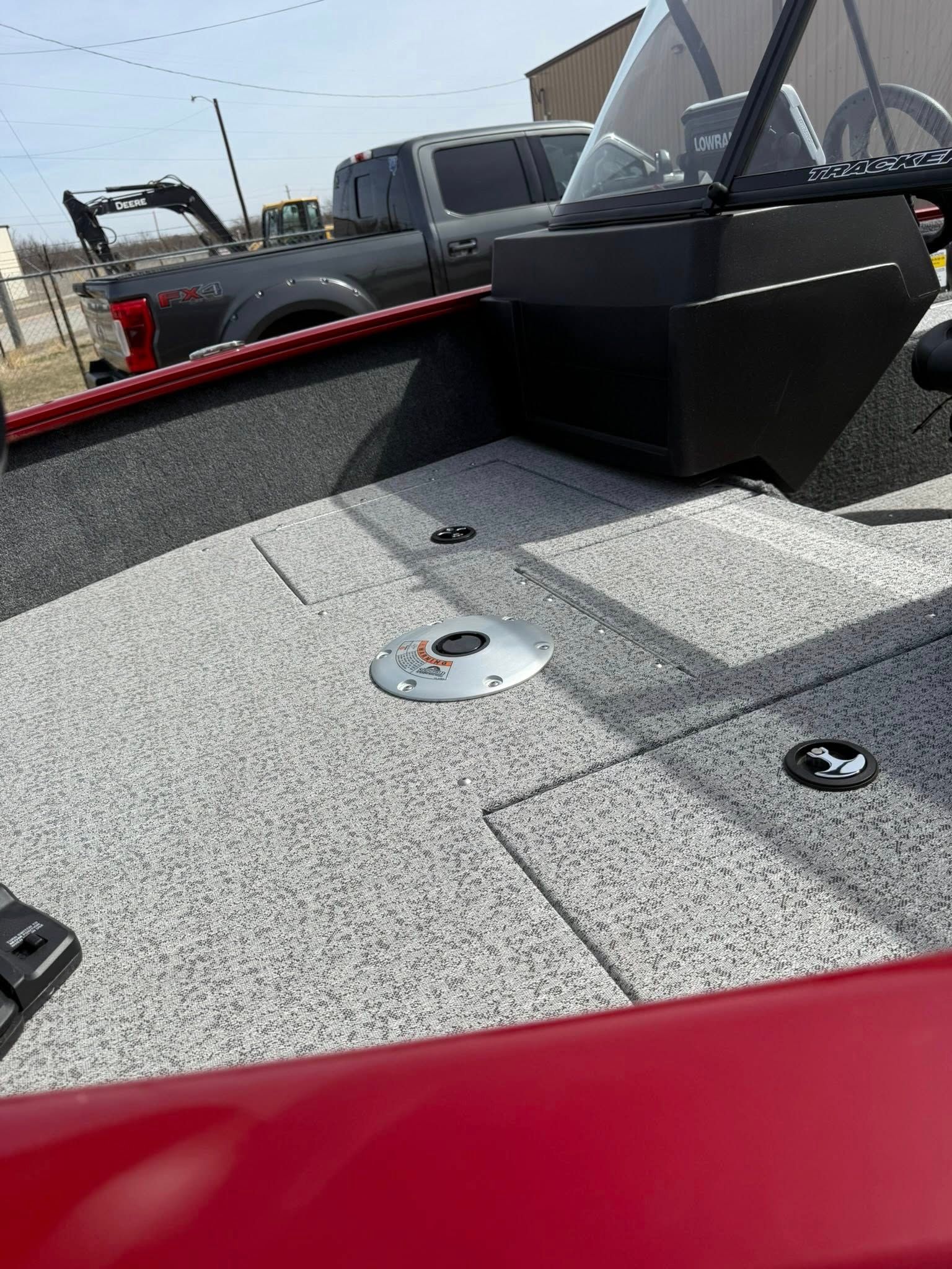 Red boat deck with gray speckled flooring, black hatch, and pickup trucks in the background.