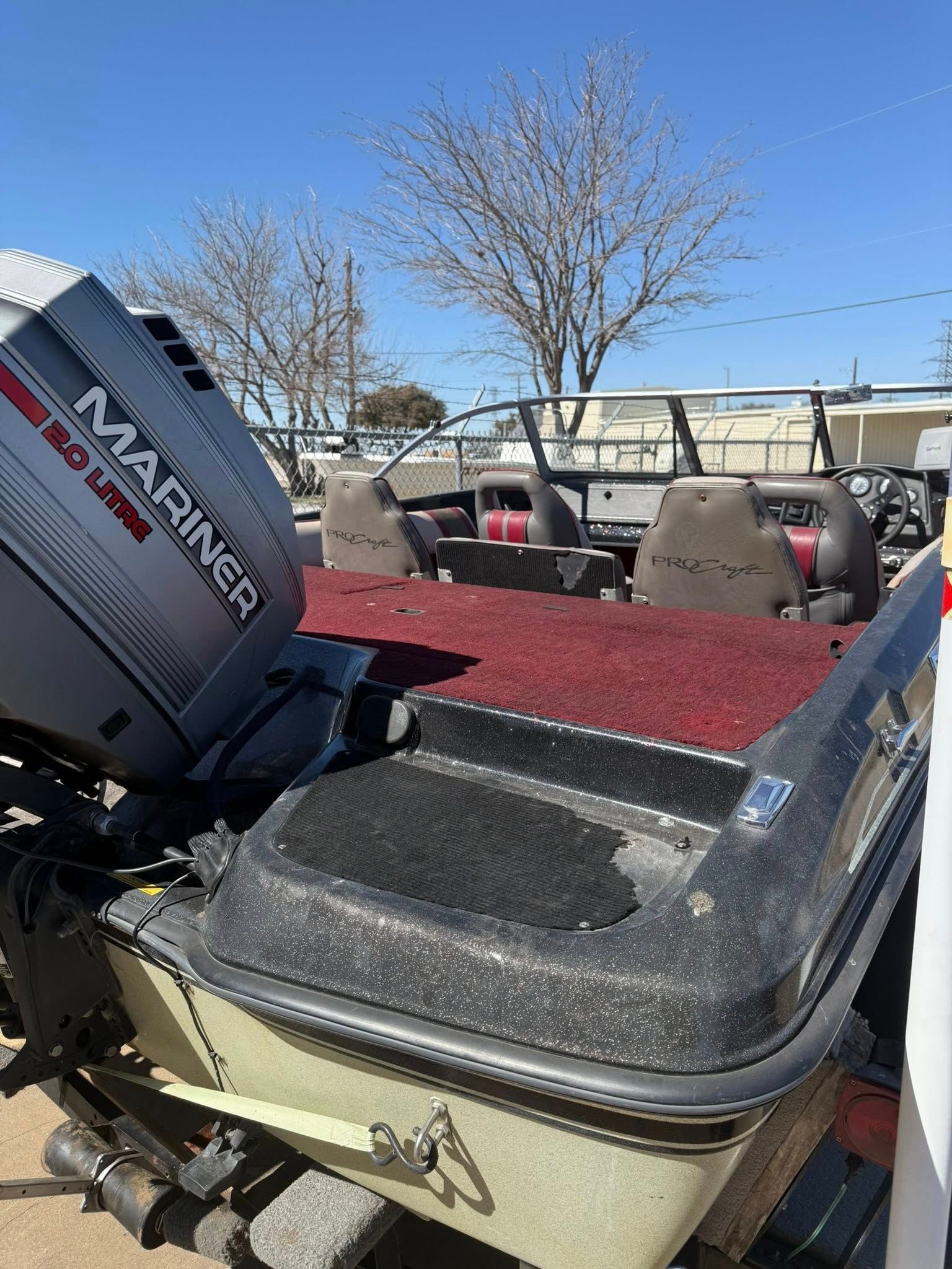 Boat stern with open tilt-outboard motor, red carpeted deck, and seats under a clear blue sky