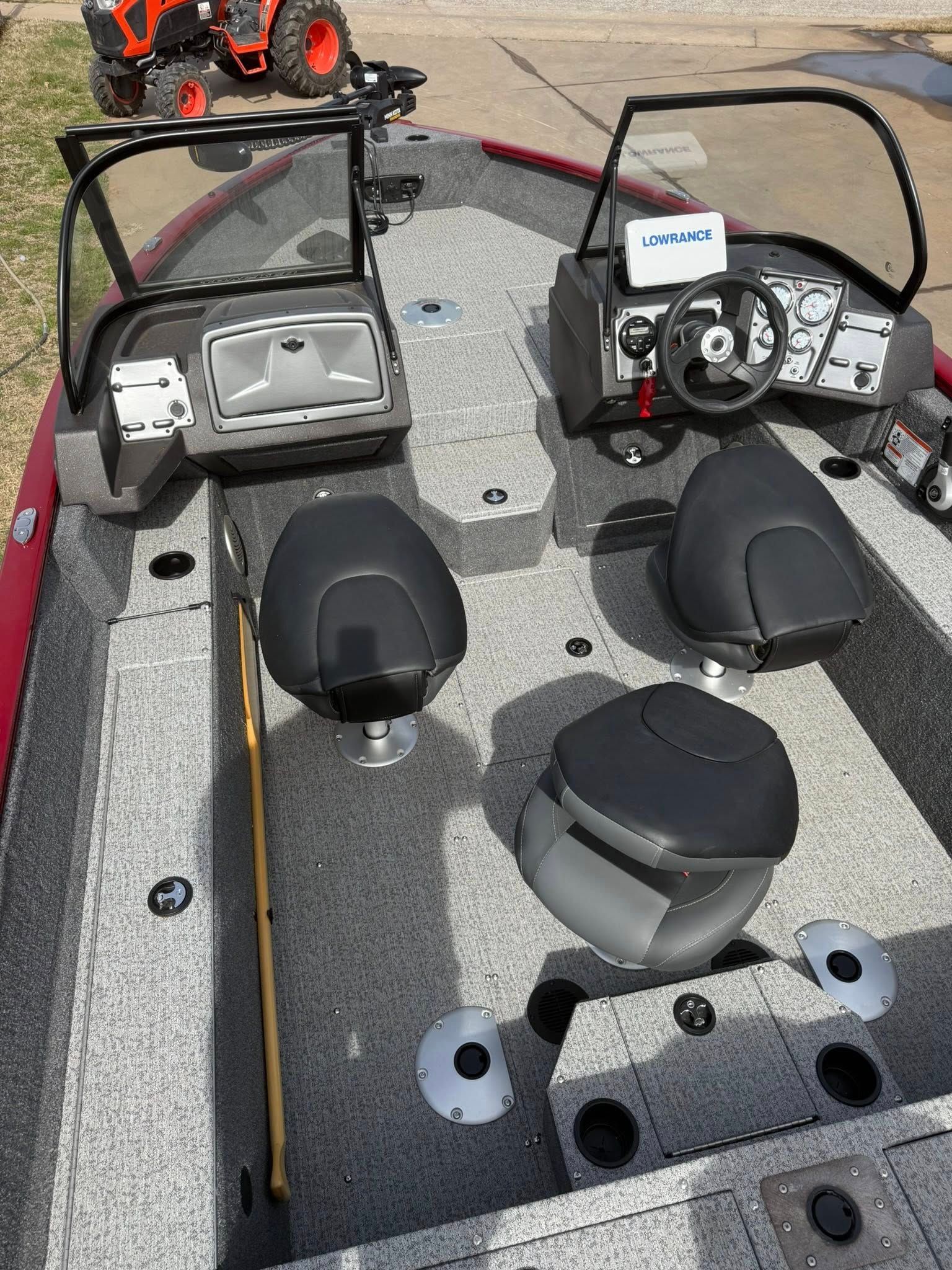 Interior of a small fishing boat with two seats, steering console, carpeted deck, and fishing rods on the bow