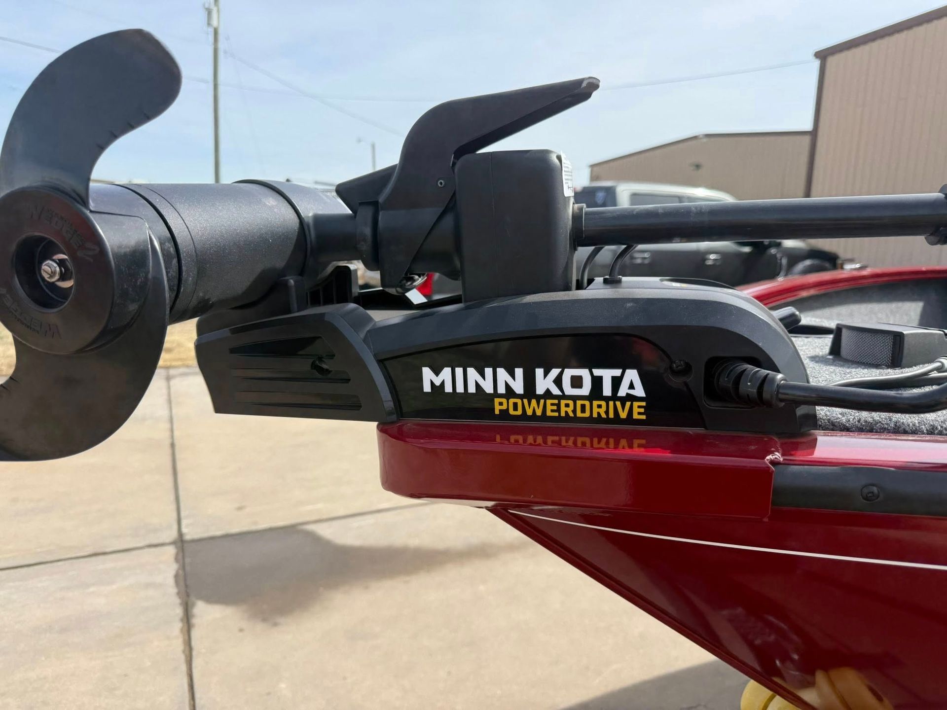 Close-up of a black Minn Kota PowerDrive trolling motor mounted on a red boat outdoors.